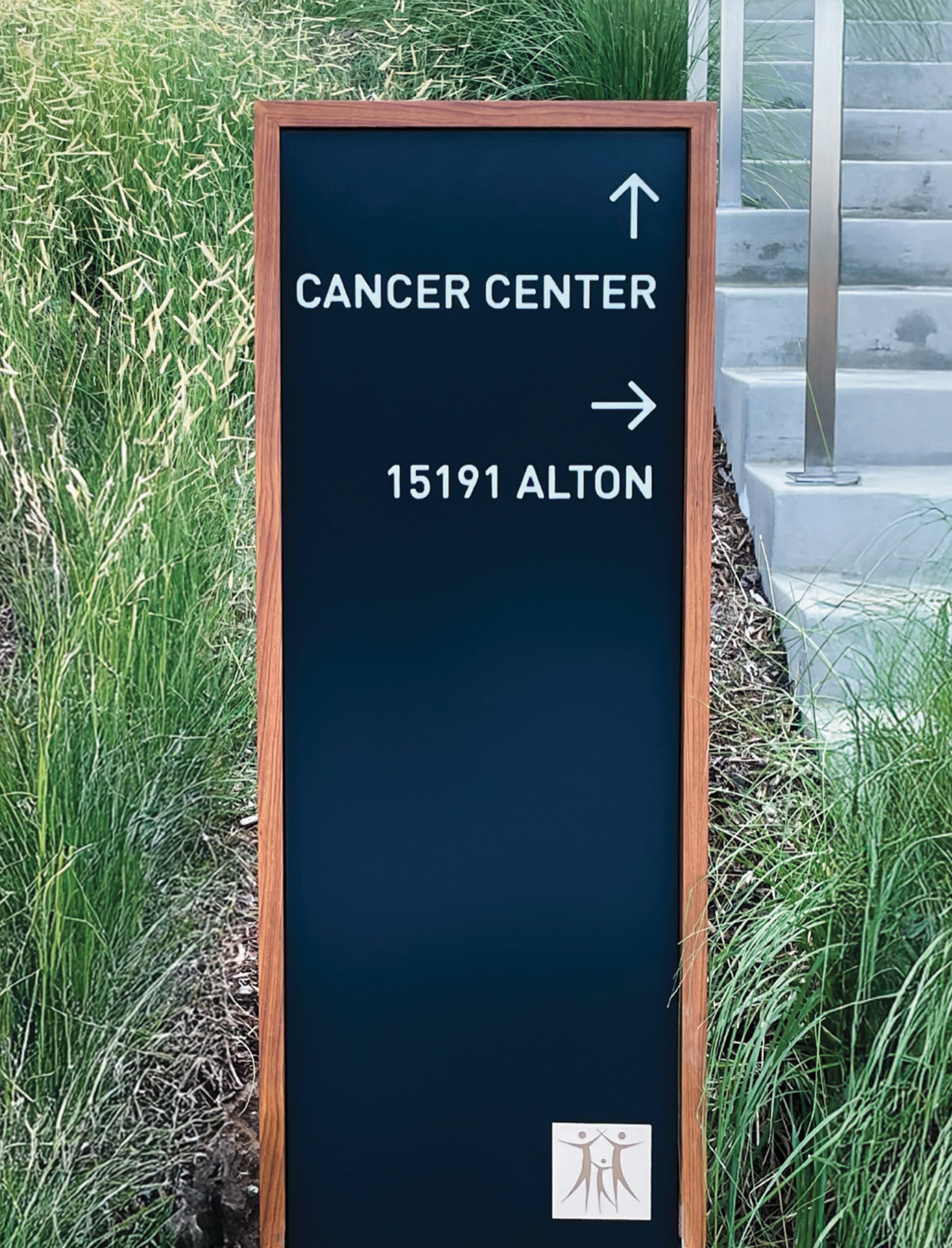 Freestanding exterior wayfinding diretional sign for a City of Hope, featuring a wood-framed panel with minimalist typography and directional arrows, integrated within a landscaped healthcare campus. Designed as part of a comprehensive environmental graphic design and signage program, the directional reflects RSM Design’s expertise in healthcare wayfinding and branded environments that enhance patient navigation, campus legibility, and the overall user experience within medical and life sciences environments.