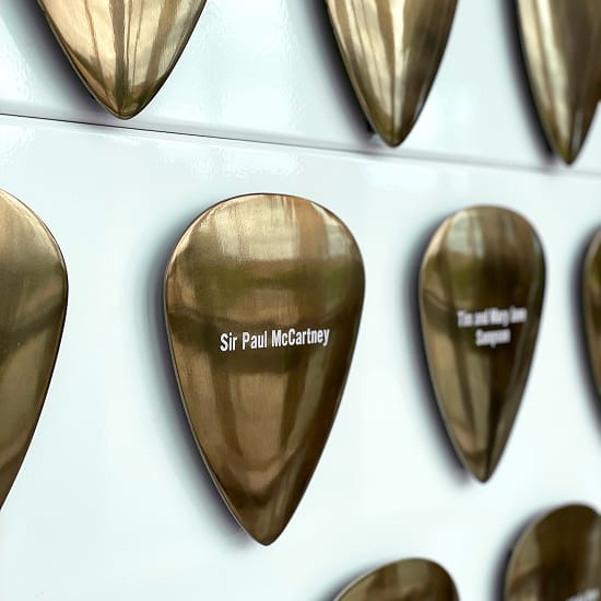 Close-up of bronze guitar pick art installation with engraved donor names including Sir Paul McCartney, commemorating Buddy Holly at the Lubbock Independent School District administrative building, Lubbock Texas