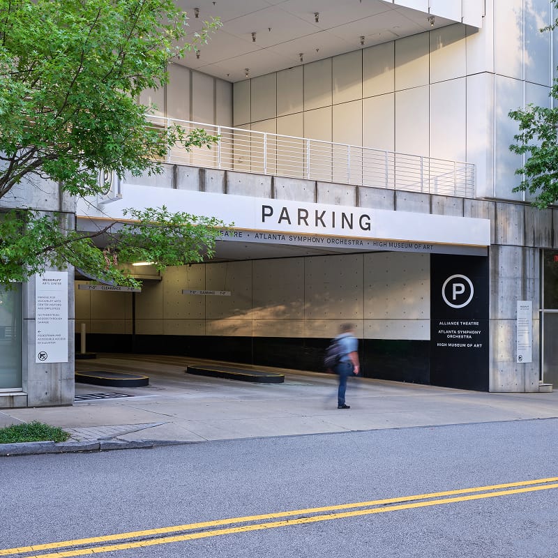 Parking garage entrance with a "PARKING" wayfinding sign, circular "P" icon, and directory listing the Alliance Theatre, Atlanta Symphony Orchestra, and High Museum of Art at the Woodruff Arts Center – campus wayfinding and environmental graphic design by RSM Design.