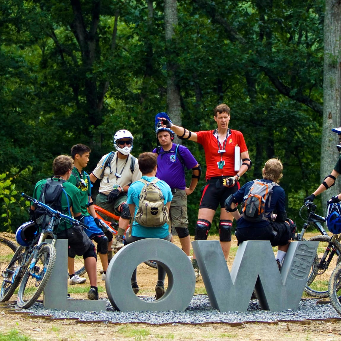 Large-scale dimensional concrete Low Gear mountain biking area letters with scouts and instructor gathered around at Summit Bechtel Reserve, experiential placemaking signage design by RSM Design