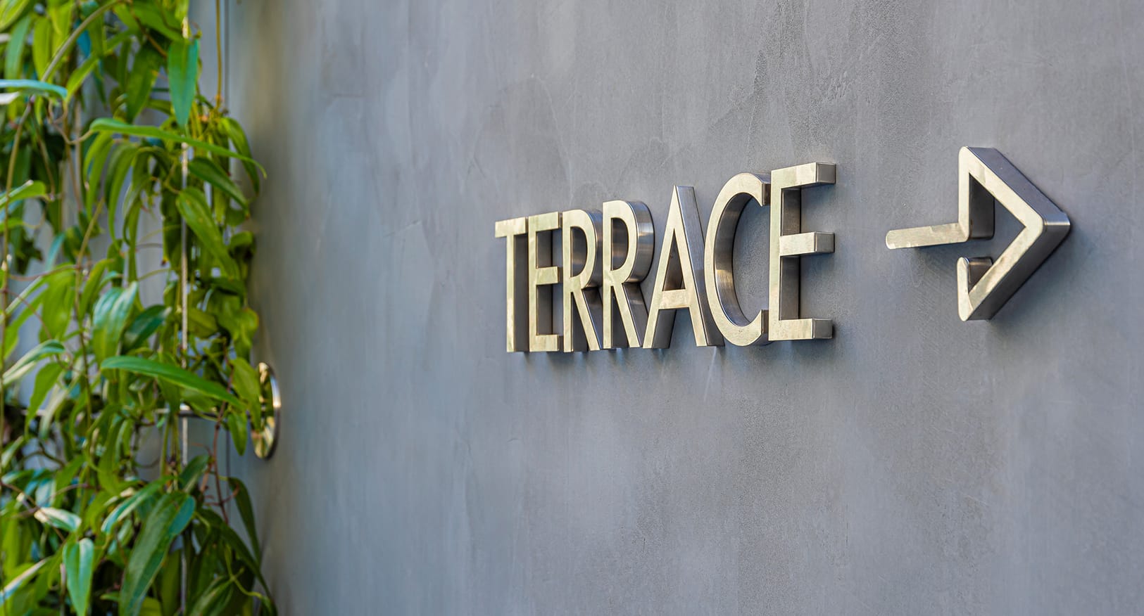 Dimensional metal terrace directional sign with arrow on concrete wall at Dallas Holocaust and Human Rights Museum - wayfinding signage by RSM Design