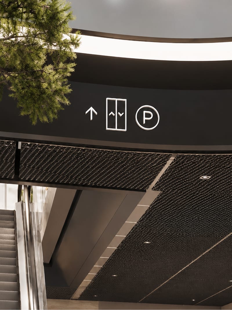 Close-up rendering of overhead pictogram signage for elevator and parking above an escalator, mesh soffit ceiling detail — wayfinding design by RSM Design