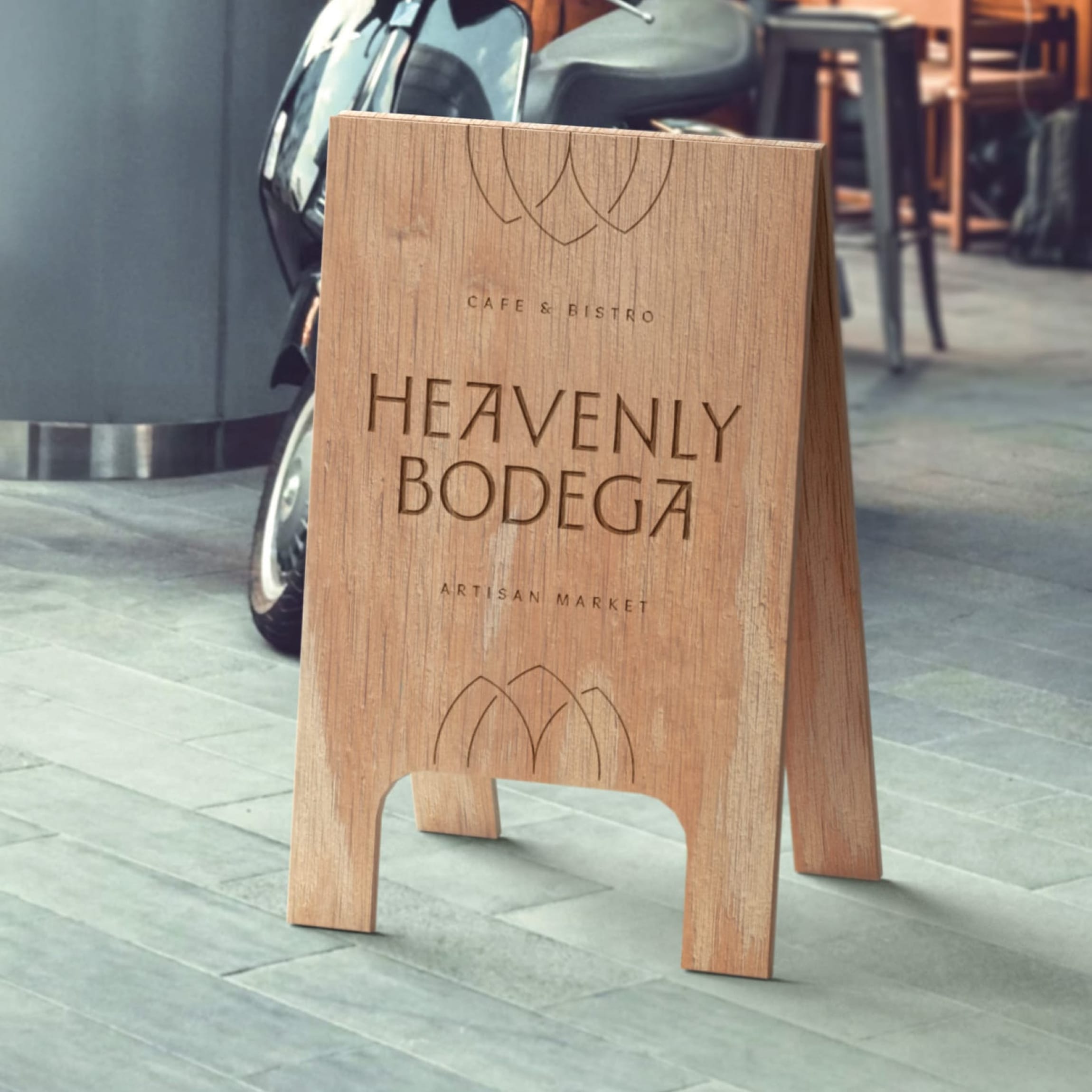 Wood A-frame sidewalk sign engraved with "Heavenly Bodega, Cafe & Bistro, Artisan Market" and tulip mark outside on a stone sidewalk — signage design by RSM Design