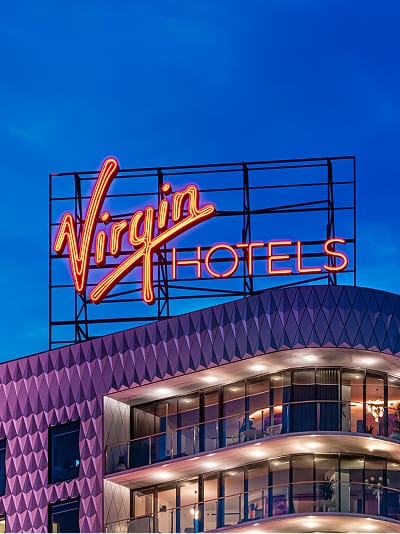 Virgin Hotels rooftop neon sign glowing against a twilight sky - large-scale rooftop signage and architectural branding design by RSM Design, a leading environmental graphics and wayfinding design firm