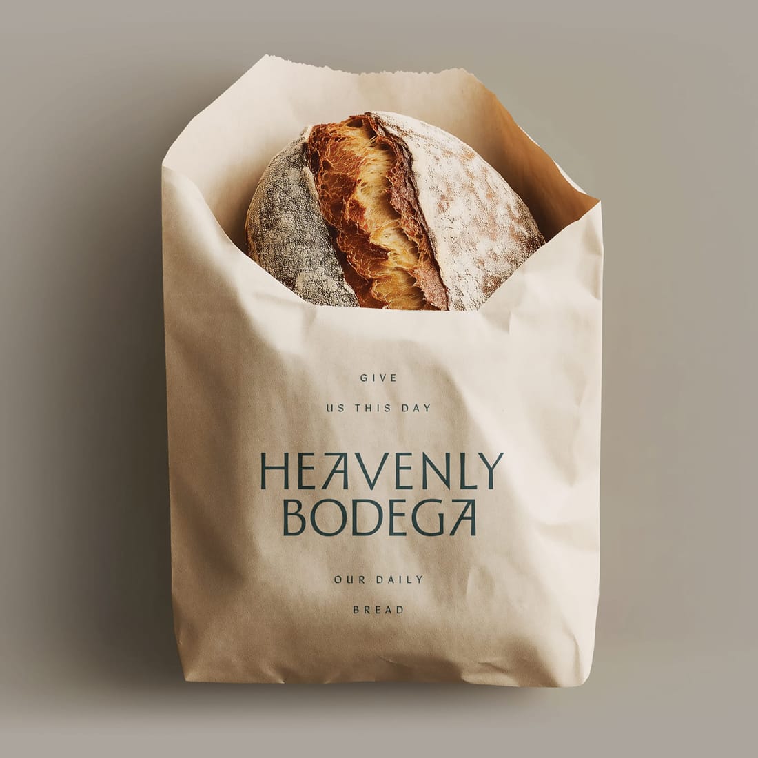 Kraft paper bakery bag printed with "Give Us This Day, Heavenly Bodega, Our Daily Bread" and a loaf of sourdough peeking out the top — packaging design by RSM Design