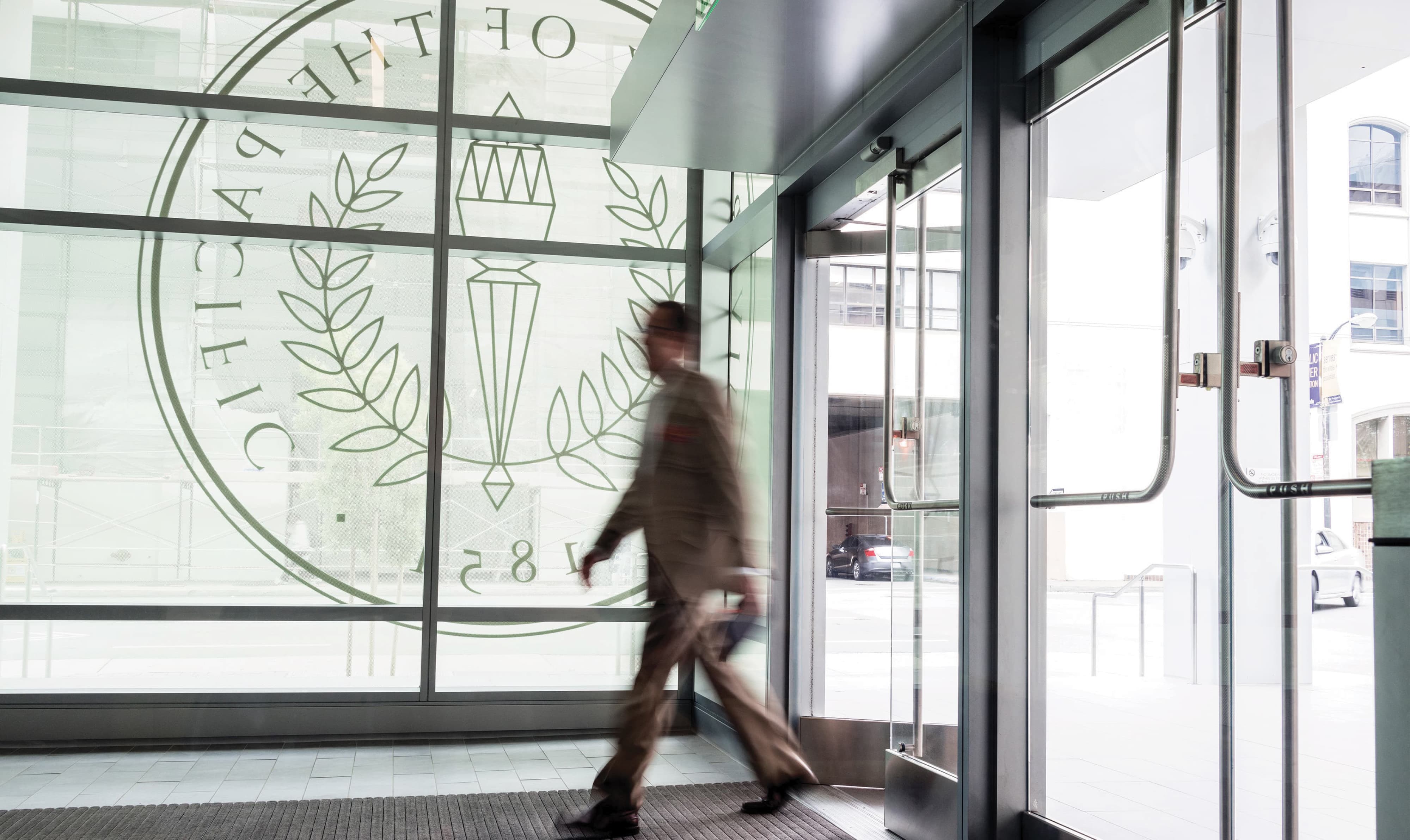 Interior lobby entry view of University of the Pacific San Francisco Campus featuring a large-scale etched glass university seal graphic established in 1851 on a floor-to-ceiling curtain wall glazing panel, with a figure in motion through the automatic door entry — RSM Design branding and visual identity, specialty graphics, experiential graphics, and environmental graphic design for education and health and wellness destinations.