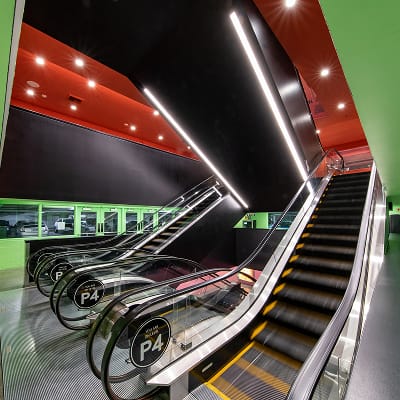 Ovation Hollywood P4 parking garage escalator bank with dramatic red and green color-coded branded environment, linear LED lighting, and circular "P4" level identification escalator cap signs