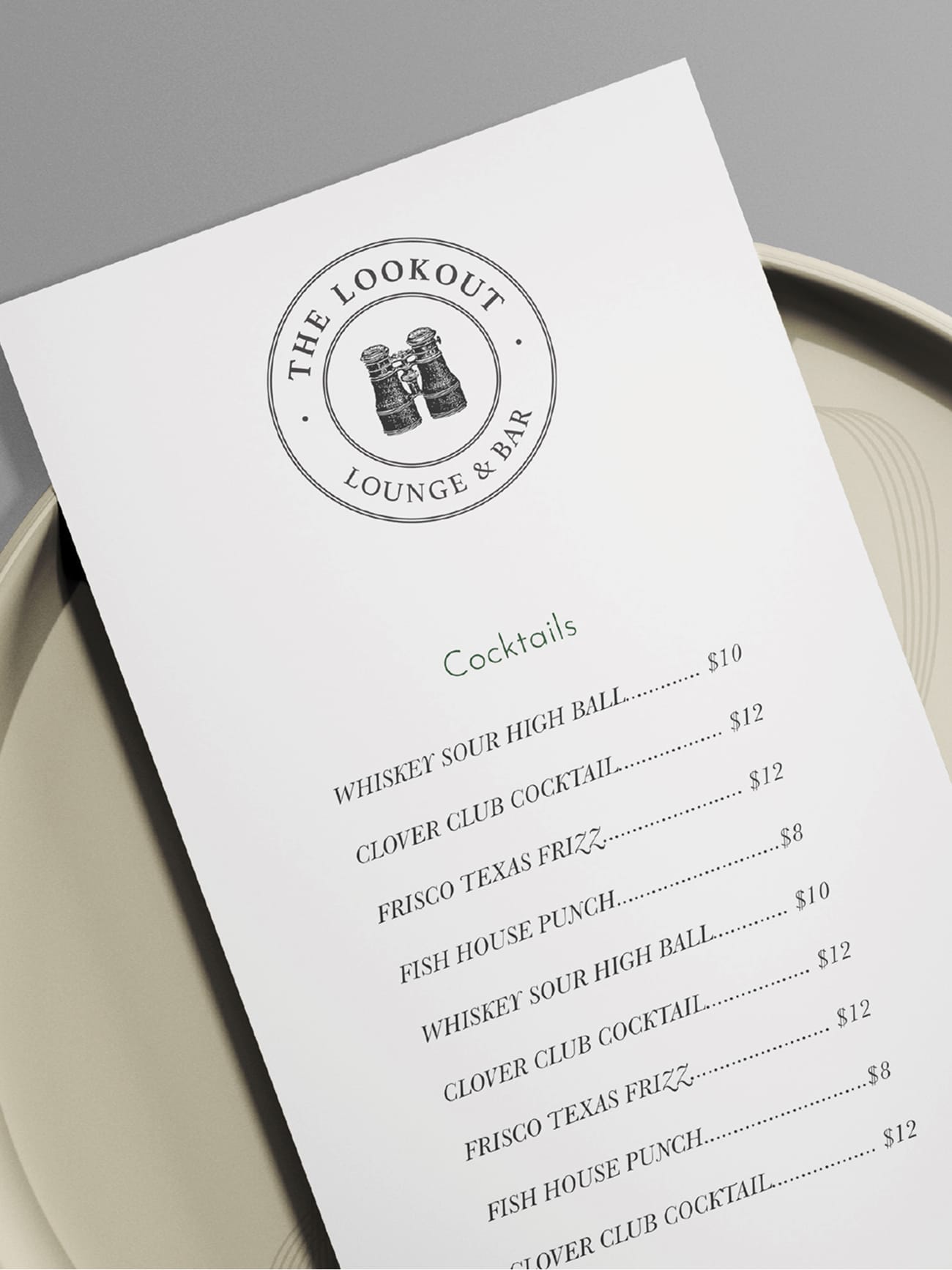 The Lookout Lounge and Bar cocktail menu with vintage binoculars circular logo and elegant typography displayed on ceramic plate, branded print collateral design at Omni PGA Frisco