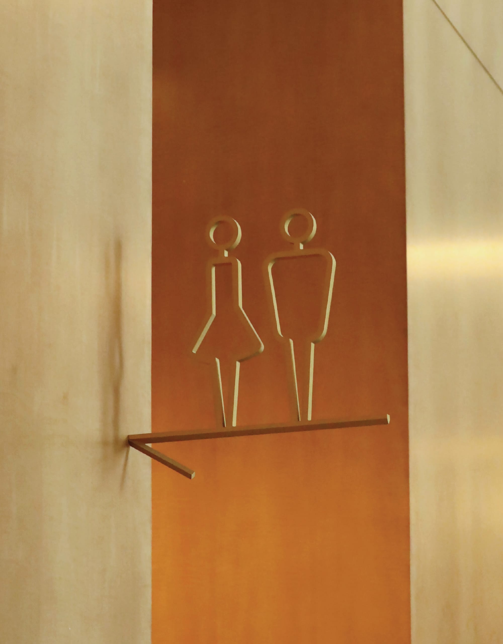 Elegant brushed copper restroom signage with modern sculptural male and female figures at The Crescent Hotel, showcasing luxury boutique hotel interior design details