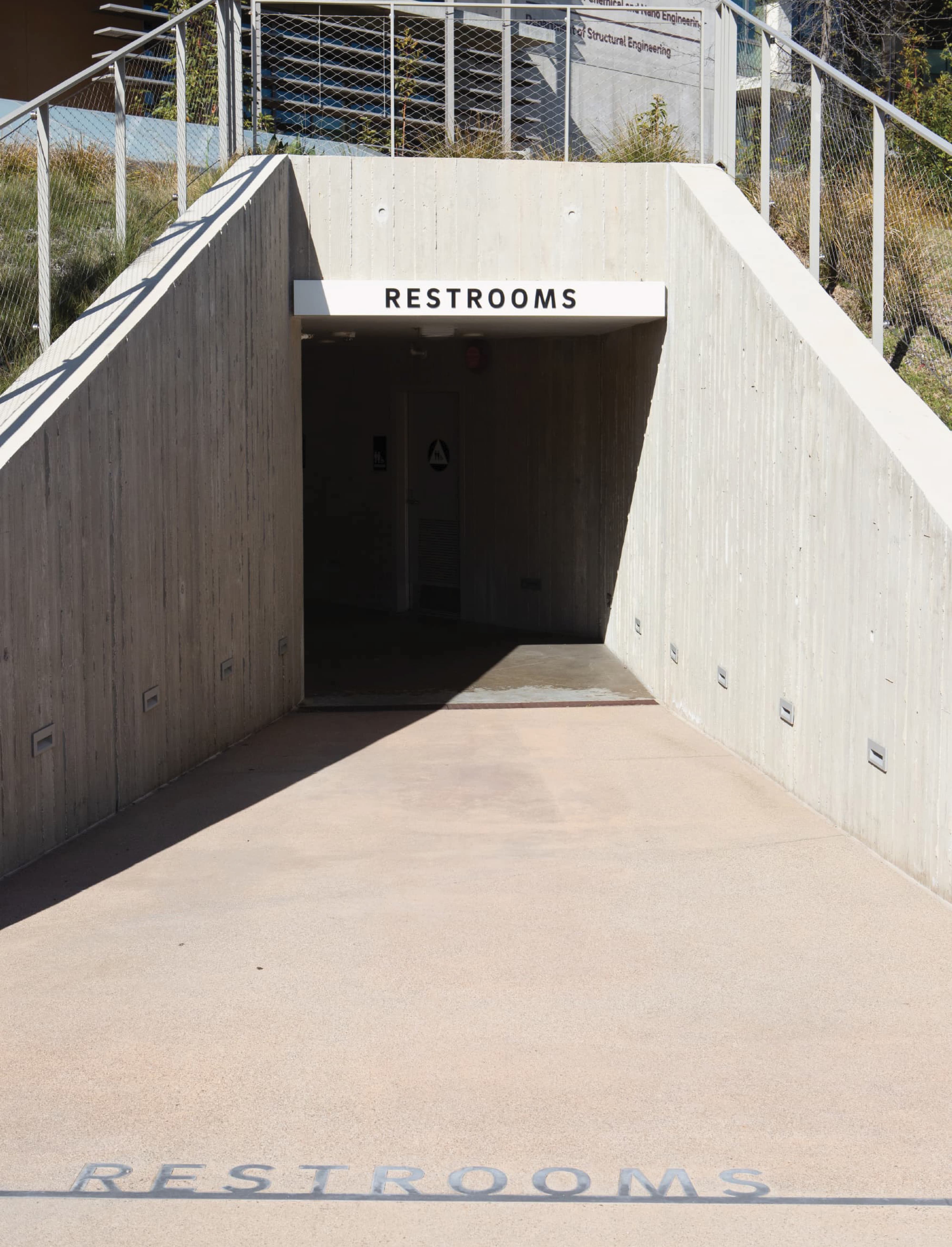 Restroom entry with integrated architectural signage and ground-applied wayfinding, illustrating environmental graphic design, signage systems, and user navigation within a public outdoor venue and mixed-use campus by RSM Design