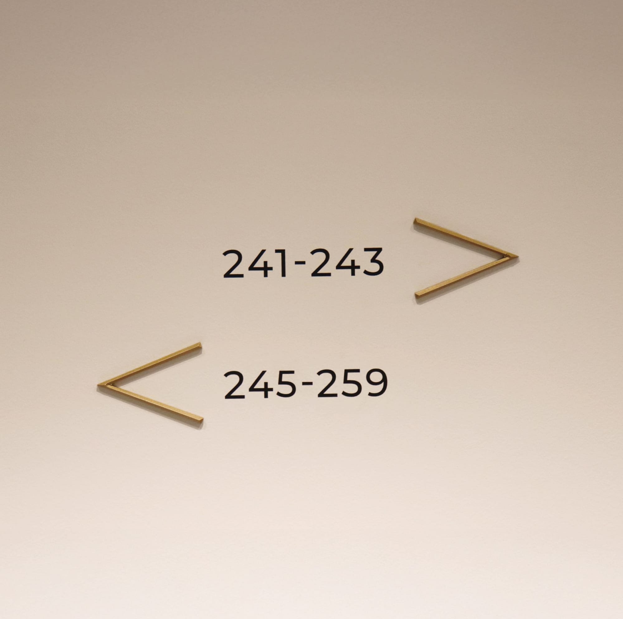 The Crescent Hotel guest room directional wayfinding signage with minimalist brass arrow indicators pointing to rooms 241-243 and 245-259 along the hotel corridor