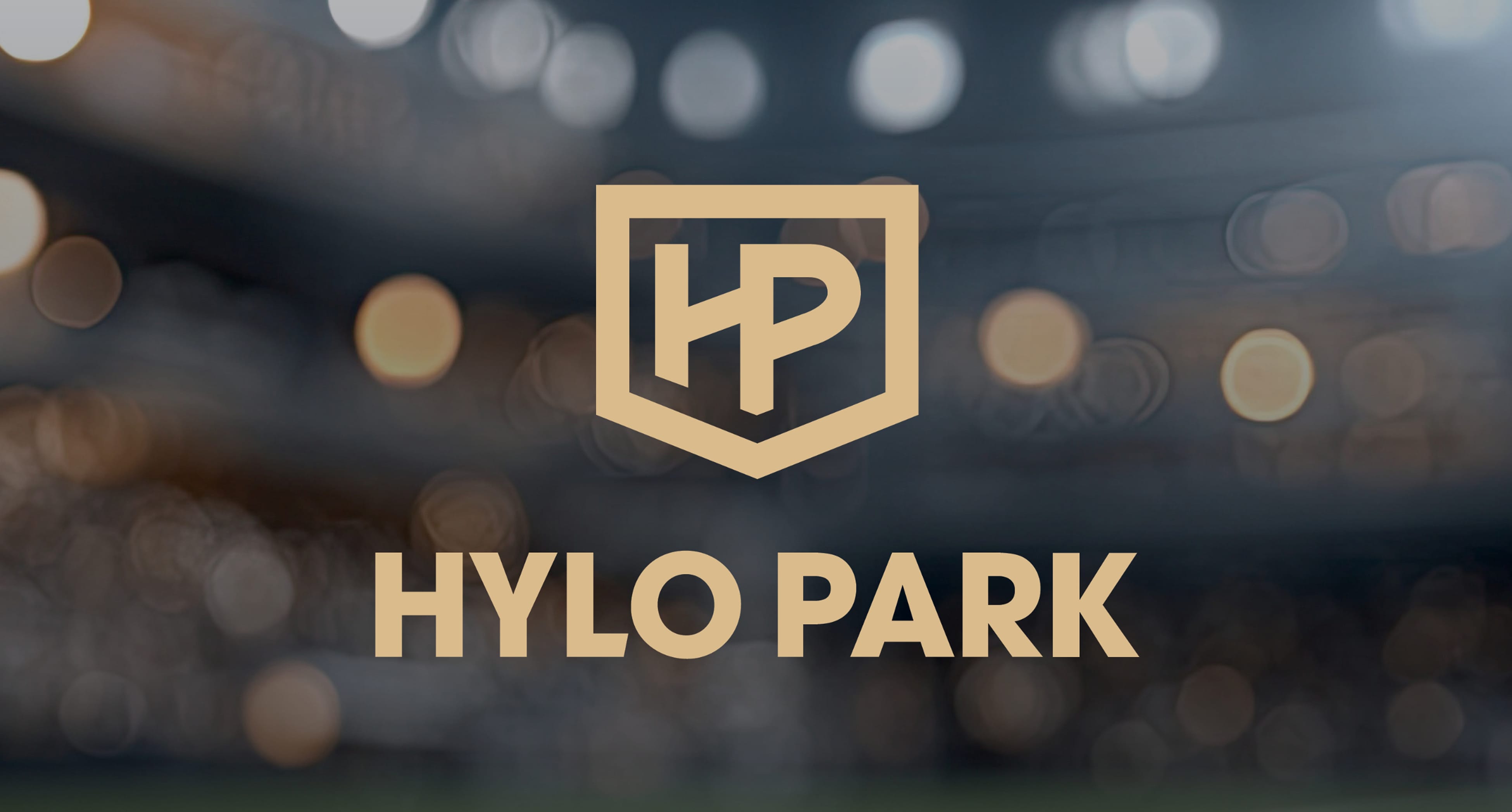 Hylo Park logo in gold, an interlocking HP monogram inside a shield above the HYLO PARK wordmark, set over a blurred background of stadium lights, Hylo Park, Las Vegas, brand identity design by RSM Design.