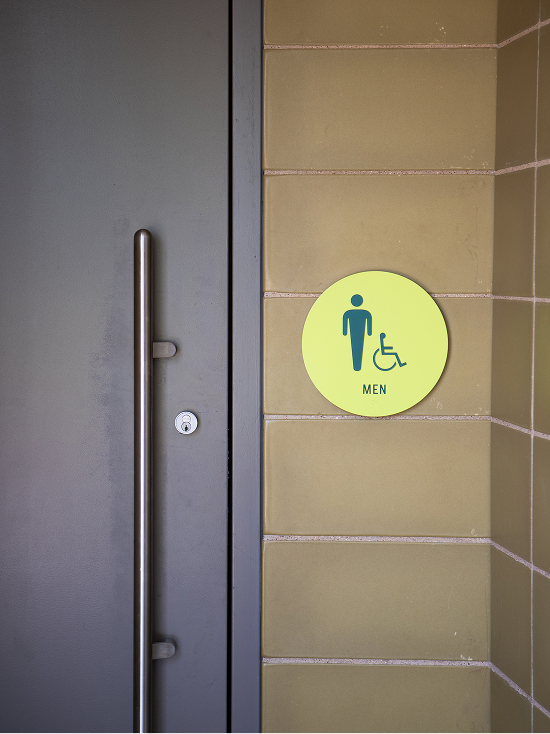 Kaleidoscope Park men's restroom ADA-accessible round lime green door sign with male and wheelchair pictograms on tan tile wall, Frisco, Texas