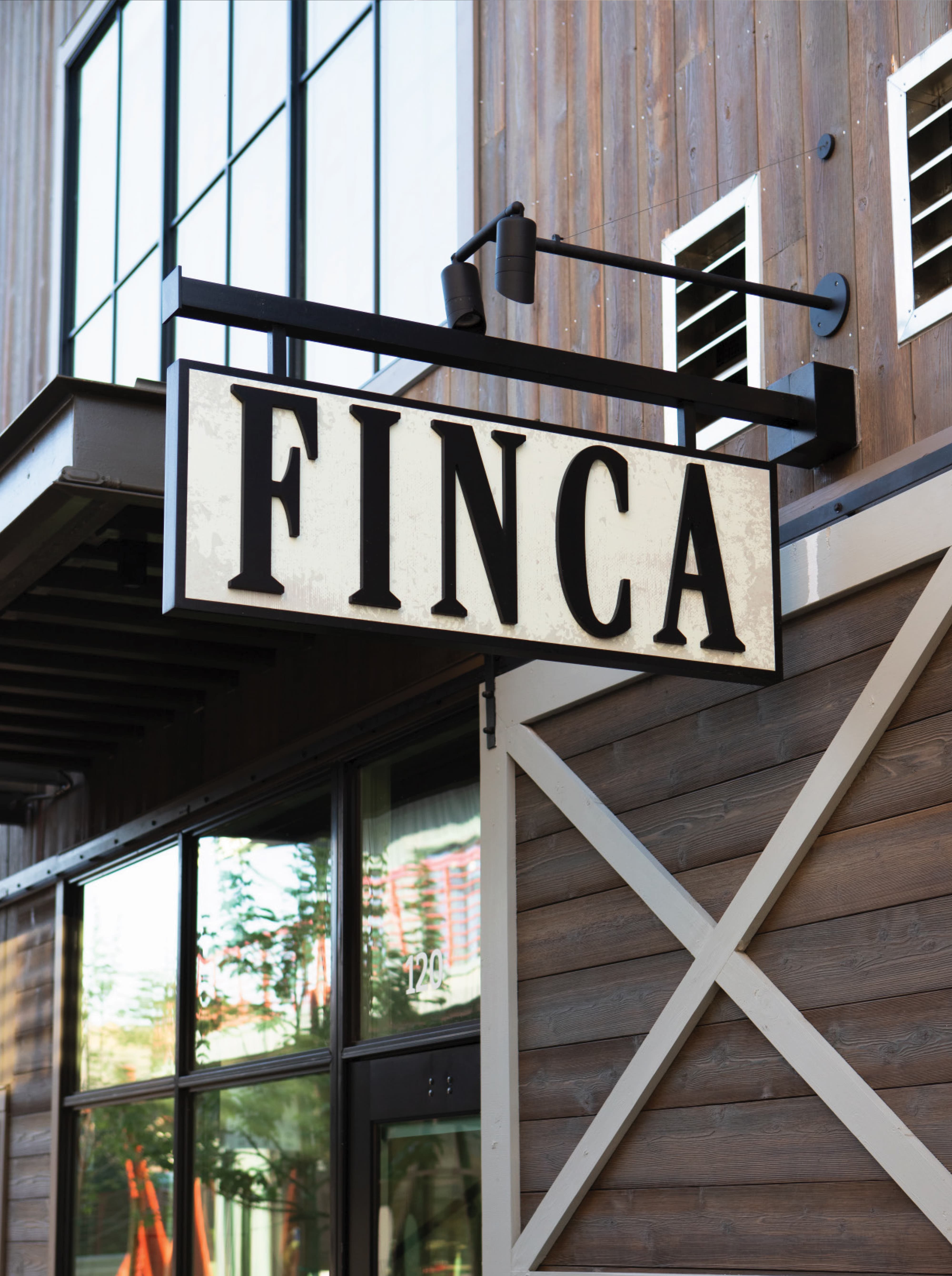 RSM Design tenant signage design for Finca at River Street Marketplace, featuring a close-up of a projecting blade sign with distressed vintage typography mounted on a wood and steel mixed-use storefront, exemplifying master sign program design and branded environmental graphics for food and beverage and retail market environments.