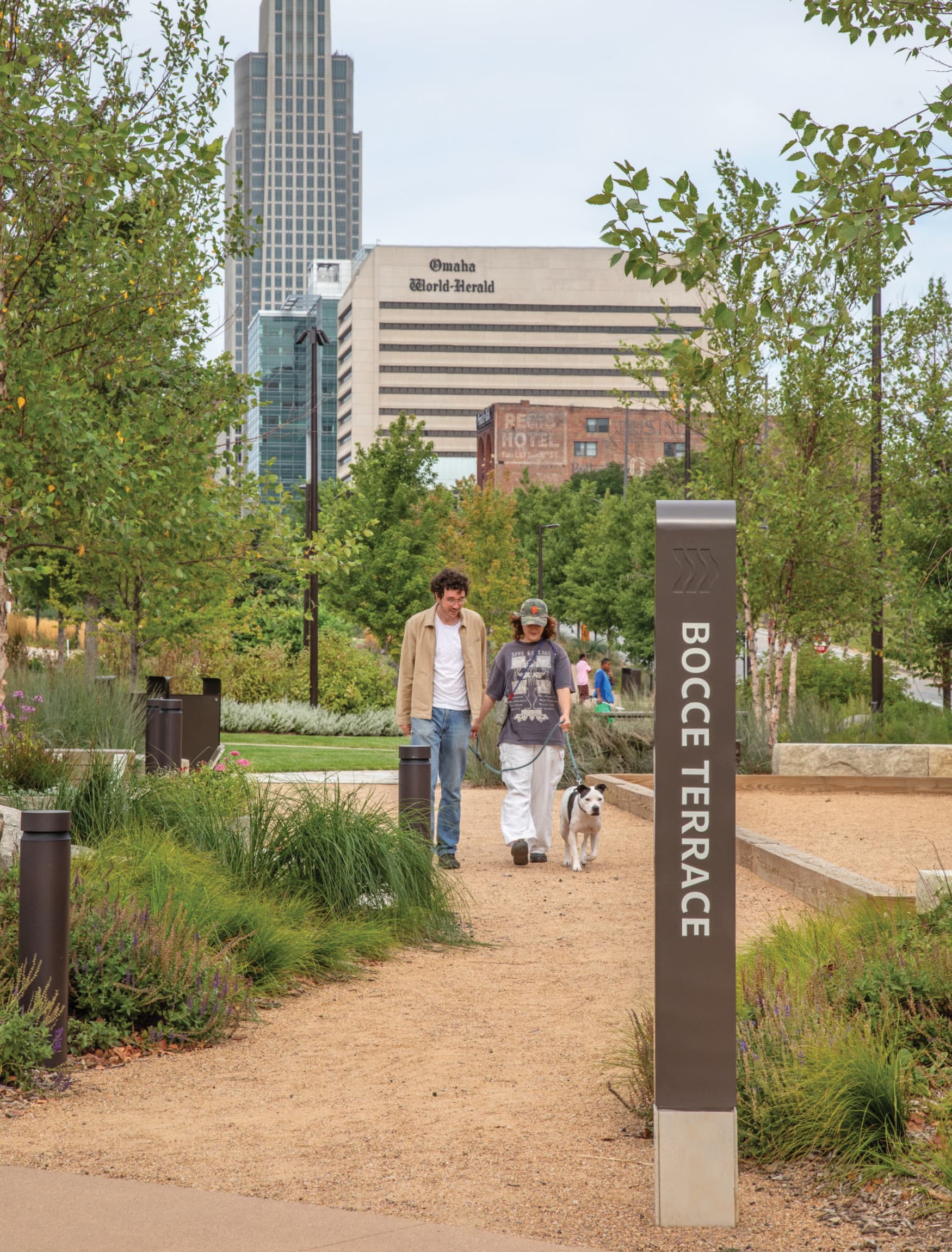 Image of two people walking their dog at the Omaha RiverFront in Omaha, Nebraska. Bocce Terrace directional pedestrian sign at the Omaha RiverFront Park. 