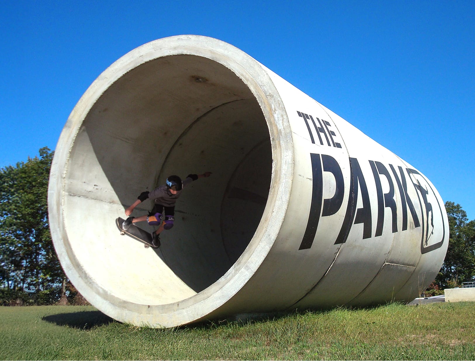 Skateboarder riding inside large concrete pipe tunnel branded with The Park signage at Summit Bechtel Reserve, large-scale recreational facility environmental graphic design by RSM Design