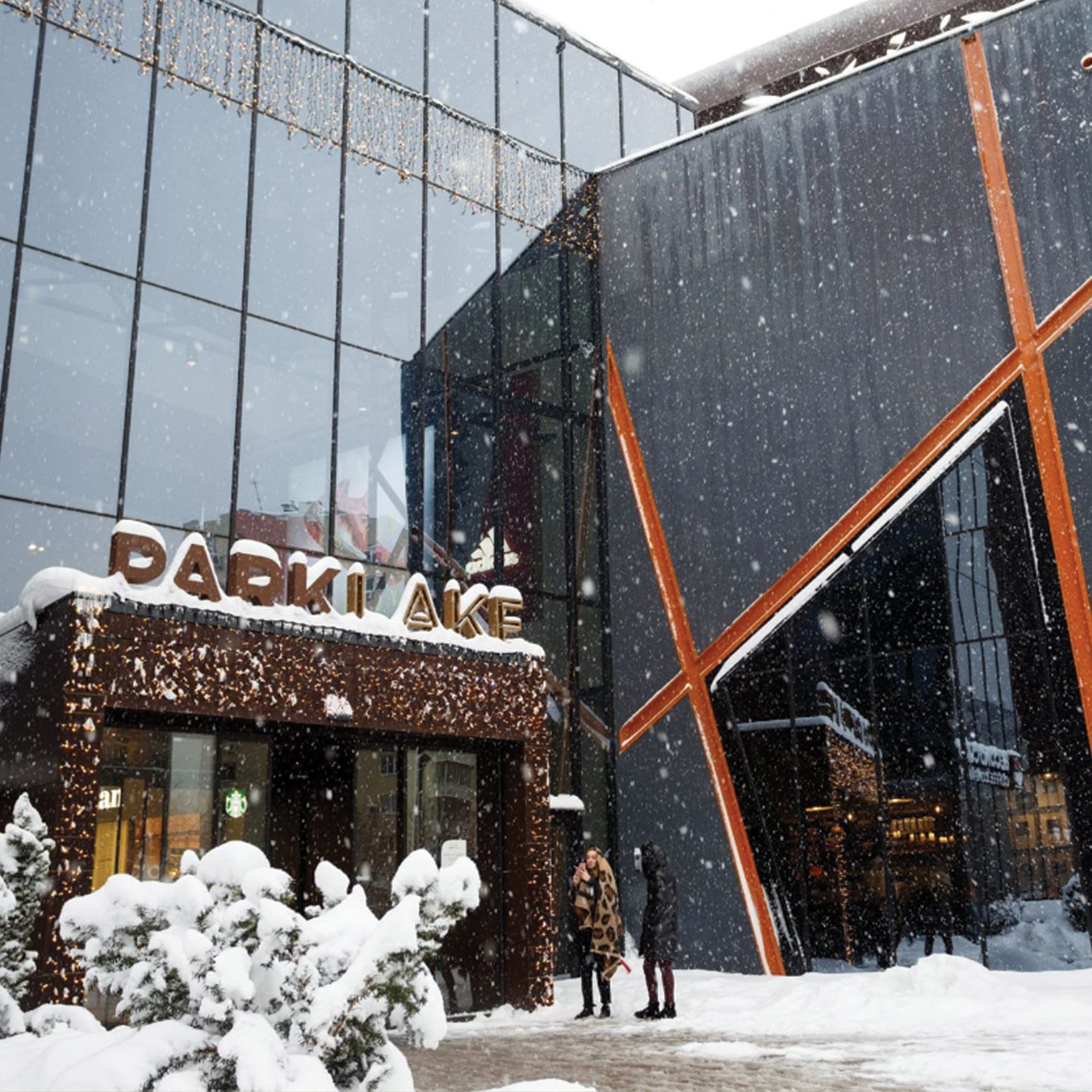 Snowy entrance of ParkLake Shopping Center in Bucharest, Romania, featuring modern glass architecture, decorative holiday lights, and snow-covered ground.