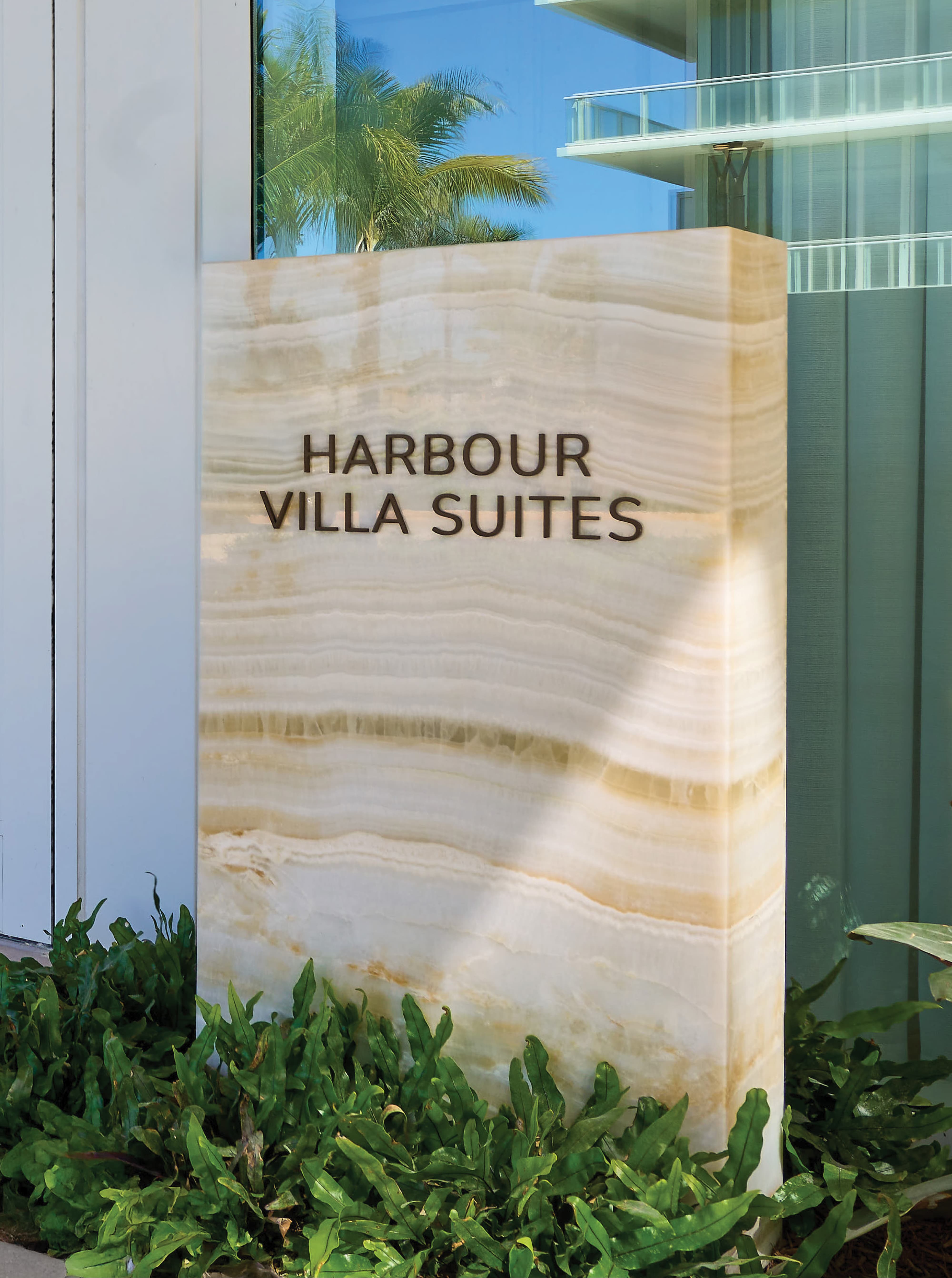 Dimensional bronze letterform "Harbour Villa Suites" identification sign mounted on a backlit onyx stone monument surrounded by tropical landscaping at Pier Sixty-Six luxury waterfront resort in Fort Lauderdale, Florida — RSM Design wayfinding and signage design, master sign programs, specialty graphics, and branded environments for hospitality, waterfront, and residential community destinations.