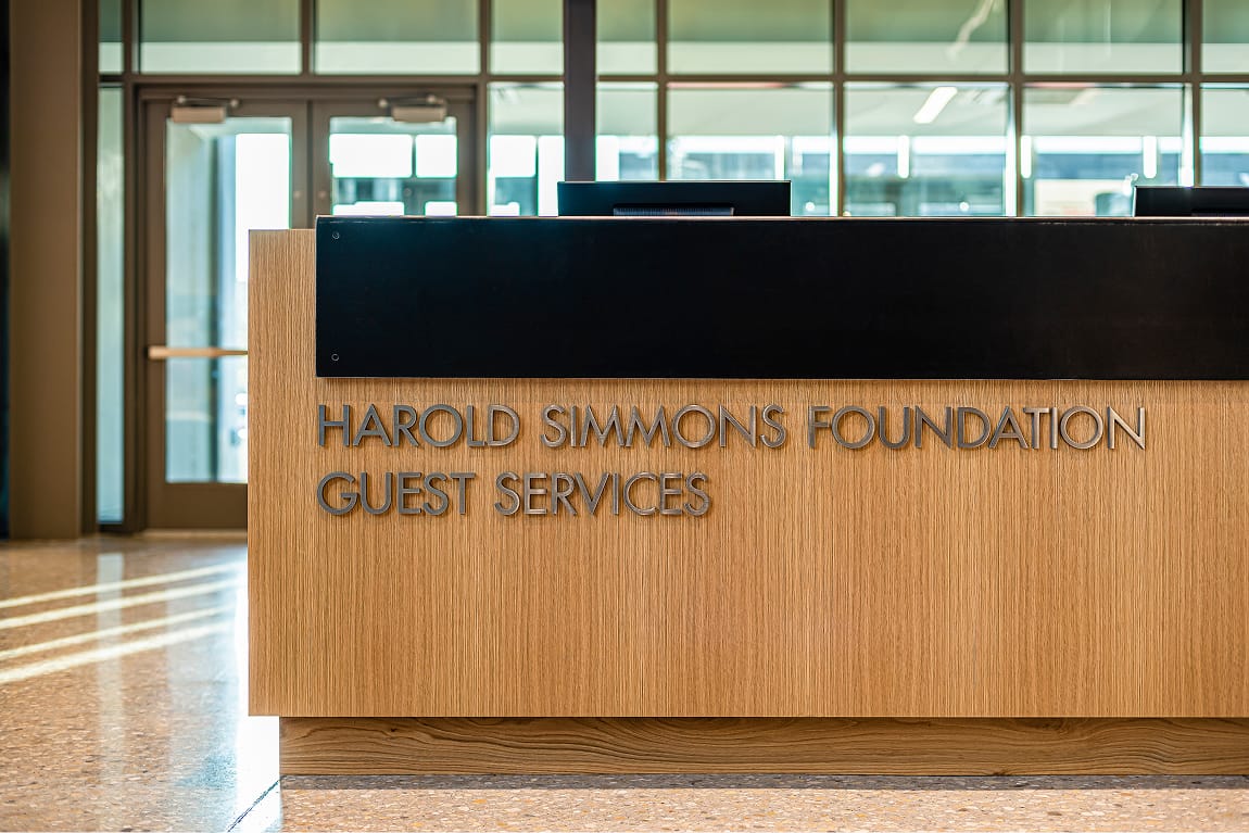 Harold Simmons Foundation Guest Services desk with dimensional wood grain signage at Dallas Holocaust and Human Rights Museum - donor recognition and wayfinding design by RSM Design