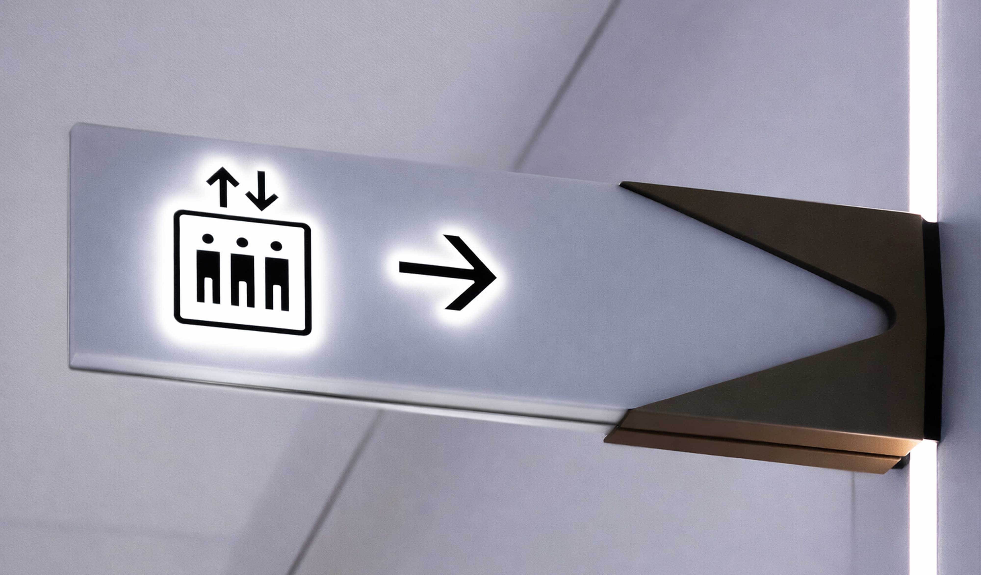 Illuminated elevator wayfinding sign with directional arrow, showcasing environmental graphic design, signage systems, and intuitive navigation that support user experience in workplace, hospitality, and mixed-use environments.