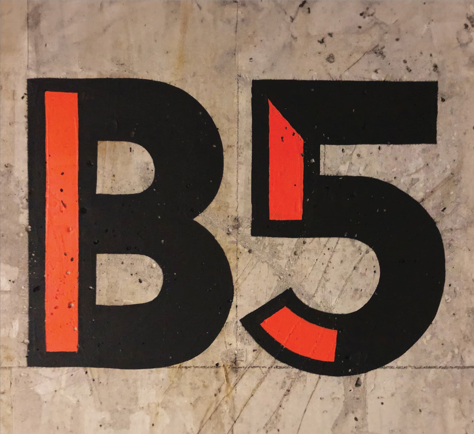 Close-up of bold black and orange painted "B5" level identifier on a raw concrete parking structure wall, showcasing wayfinding and signage design for a parking garage environment by RSM Design.