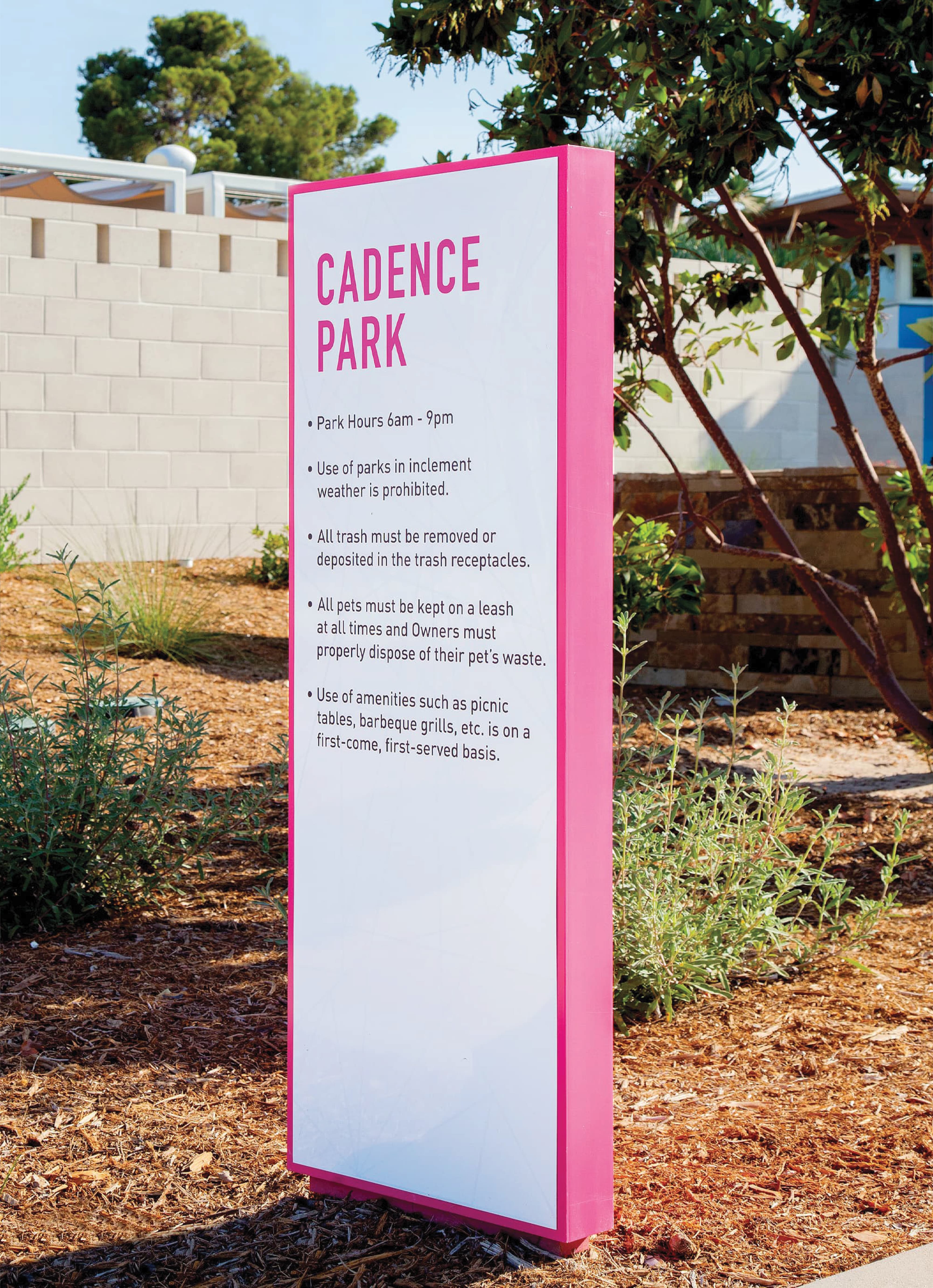 Outdoor regulatory signage totem for Cadence Park with bold pink branding and park rules text, demonstrating wayfinding and signage design for residential community and park environments by RSM Design.