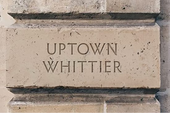 Uptown Whittier engraved stone signage featuring refined serif typography, integrating the district identity into historic architectural elements.