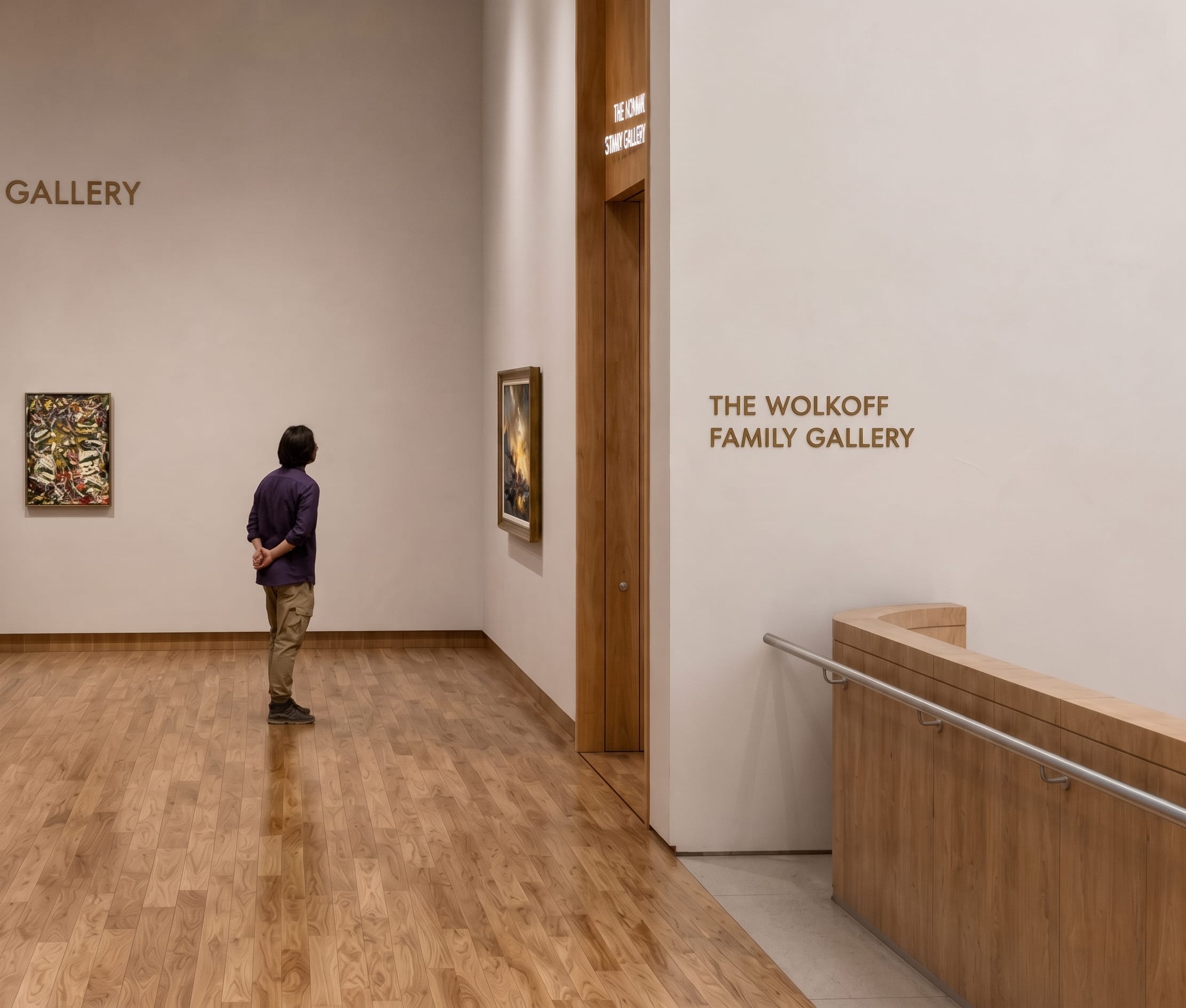 Bronze dimensional lettering reading "The Wolkoff Family Gallery" beside a wood-framed doorway in an art gallery corridor, donor recognition signage by RSM Design