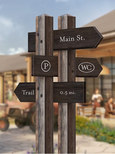 Weathered wood directional signpost with arrow markers for Main St, parking, restrooms, and trail, wayfinding by RSM Design.