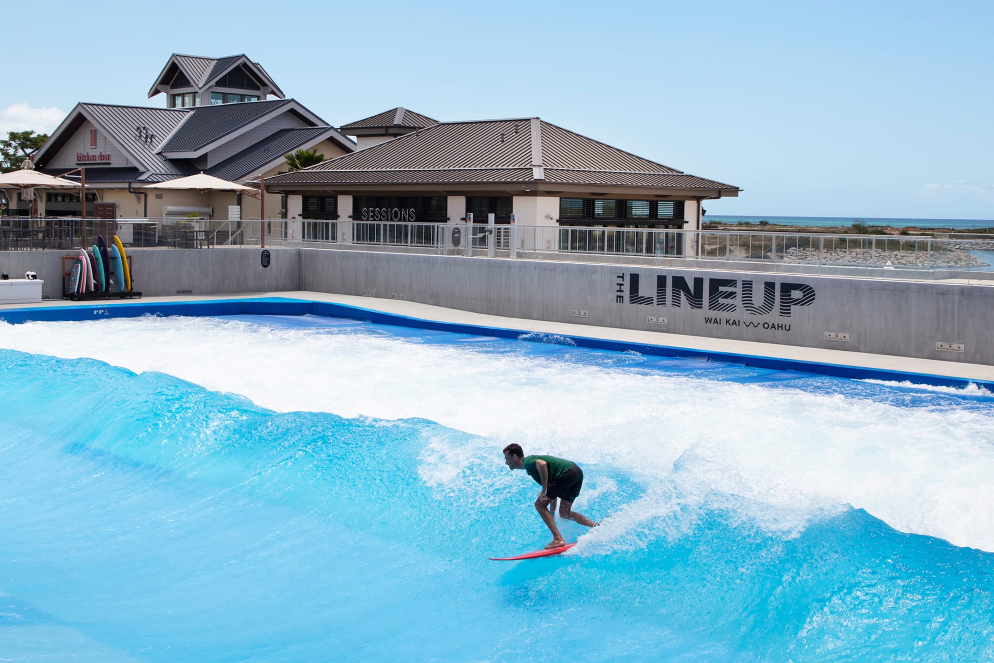 Surfer riding wave beneath "The Lineup" wall signage with Sessions and Kitchen Door buildings at Wai Kai, Ewa Beach, Oahu, environmental graphic design by RSM Design.