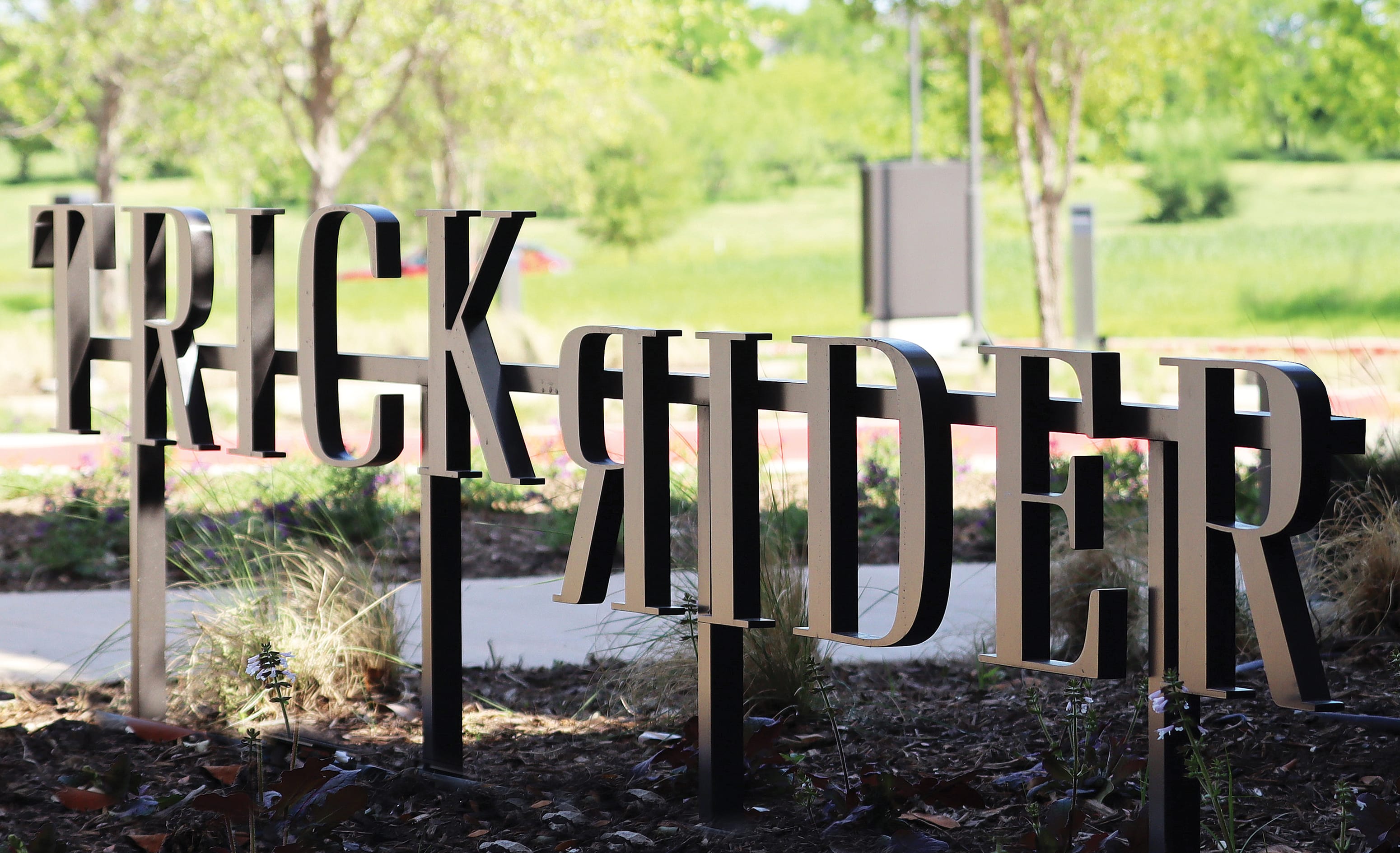 Trick Rider dimensional letter signage staked in garden bed along a walking path, Omni PGA Frisco Resort, environmental graphic design by RSM Design.