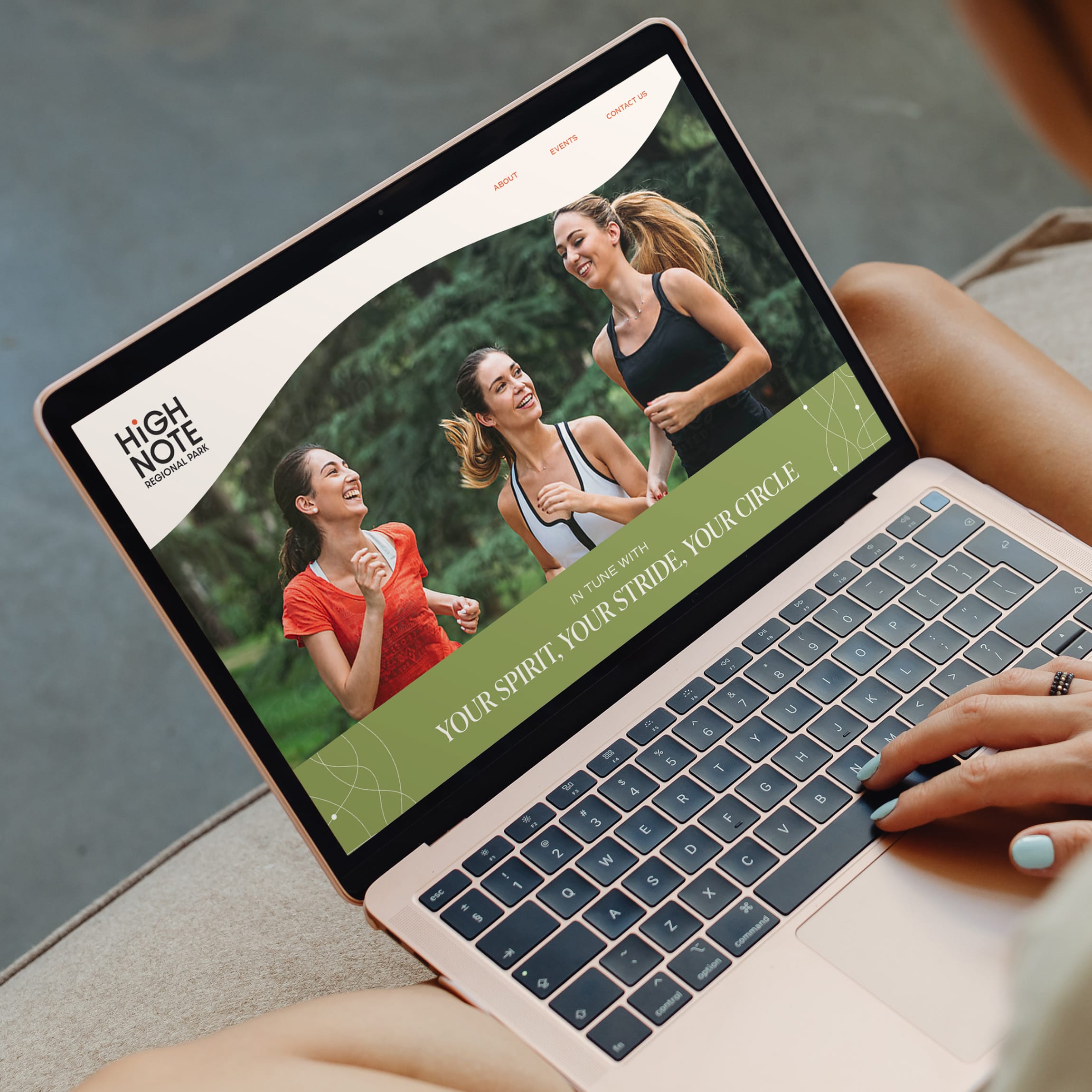 Laptop mockup on a person's lap displaying the HighNote Regional Park website homepage, showing three women running and laughing together beside the tagline "Your Spirit, Your Stride, Your Circle" — website design by RSM Design.