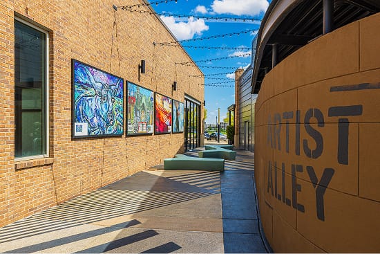 Artist Alley outdoor public art corridor at Toyota Music Factory mixed-use entertainment district in Irving, Texas, featuring curated art panels, experiential graphics, and specialty environmental lettering — RSM Design art programs, public art, placemaking, and branded environments for mixed-use, food and beverage, streetscape, and cultural destinations.


