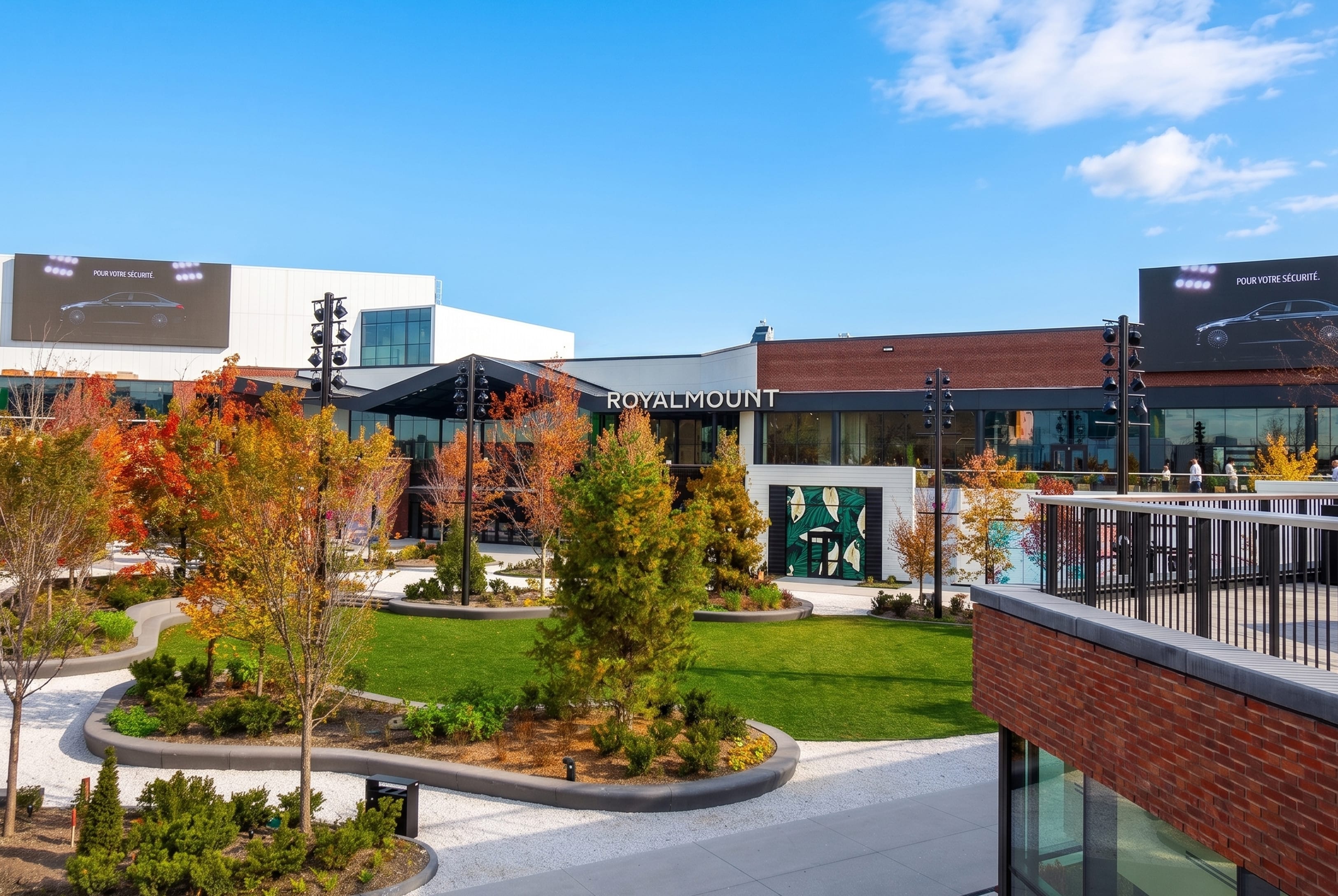 Exterior plaza at Royalmount with dimensional building signage, landscaped lawn and fall foliage, and large digital ad screens on either side — placemaking and signage design by RSM Design