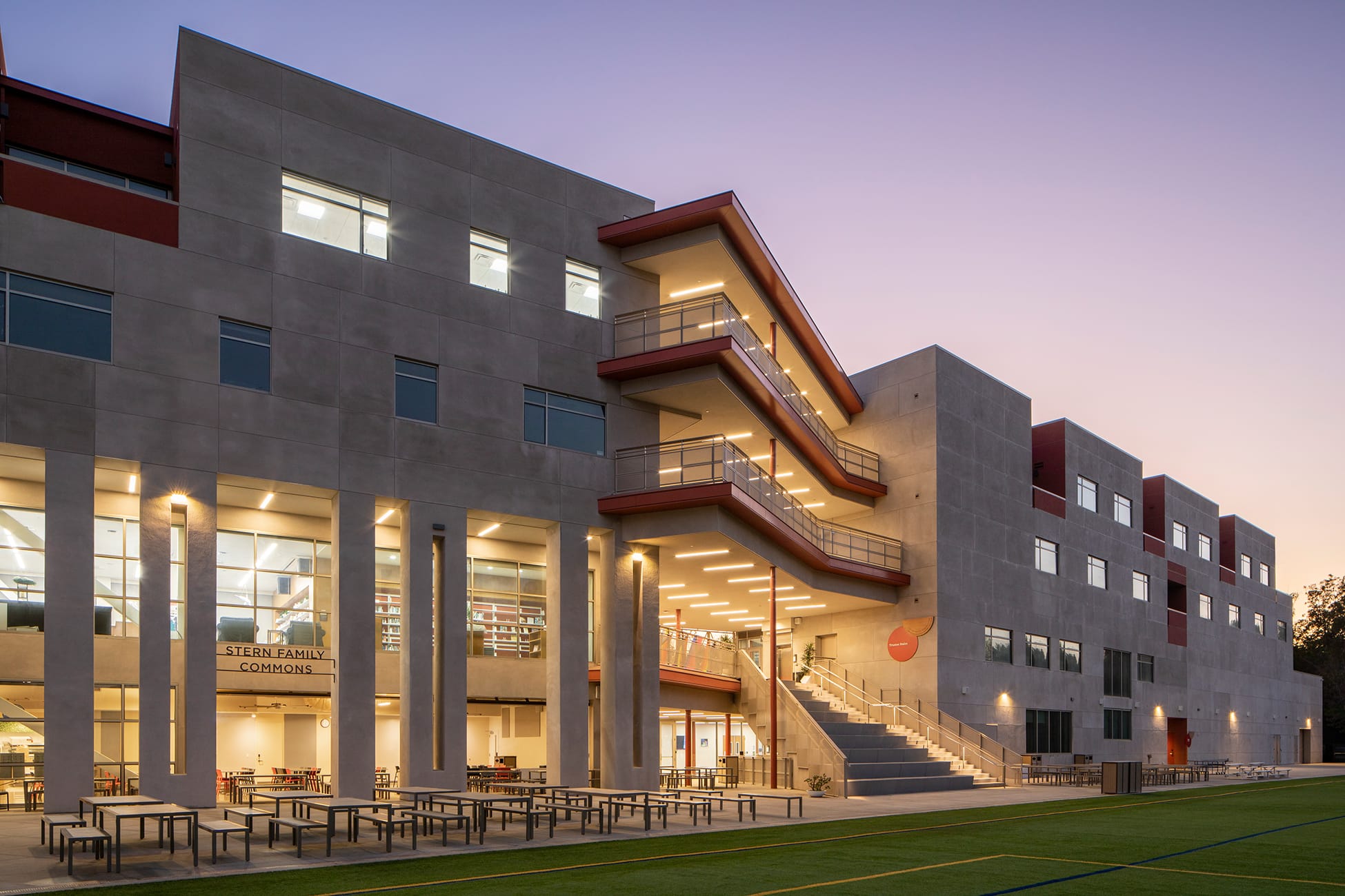 Stern Family Commons illuminated at twilight with tiered balconies overlooking athletic field at Brentwood School campus in Los Angeles - donor recognition and environmental graphic design by RSM Design