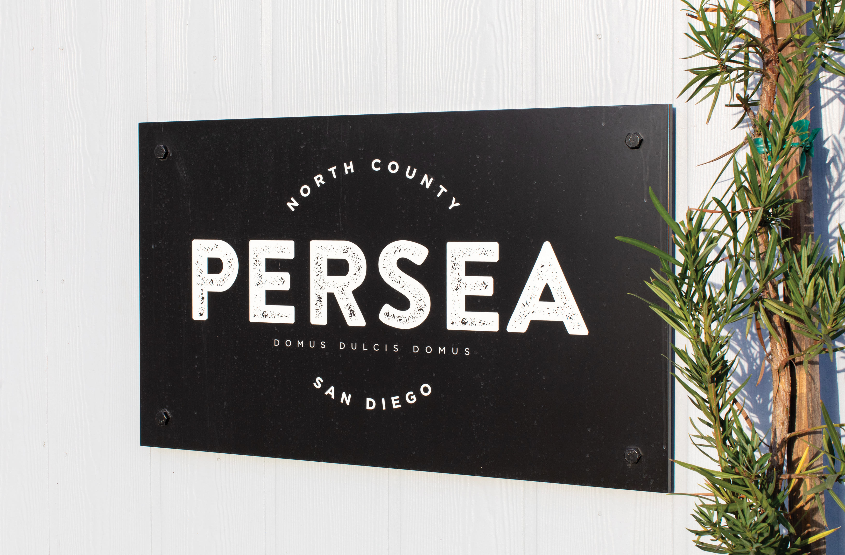 Black horizontal plaque with visible fastners and white Persea logo and text. Signage and wayfinding for Persea in San Diego, California by RSM Design