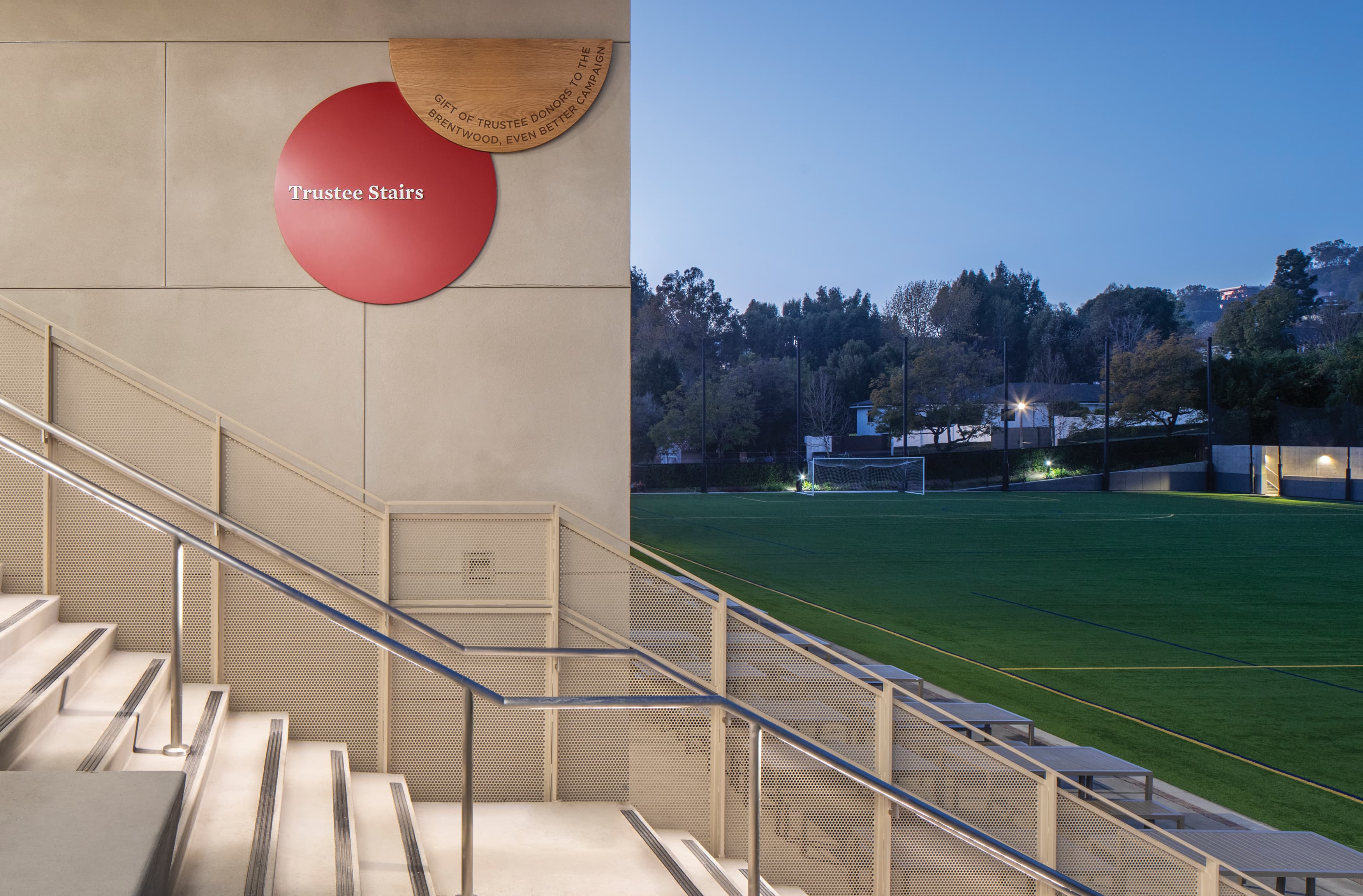 Trustee Stairs wayfinding graphic signage with bold red with white lettering behind warm wooden signage. Donor signage for Brentwood School in Los Angeles by RSM Design. Stairway signage near soccer field at middle school.