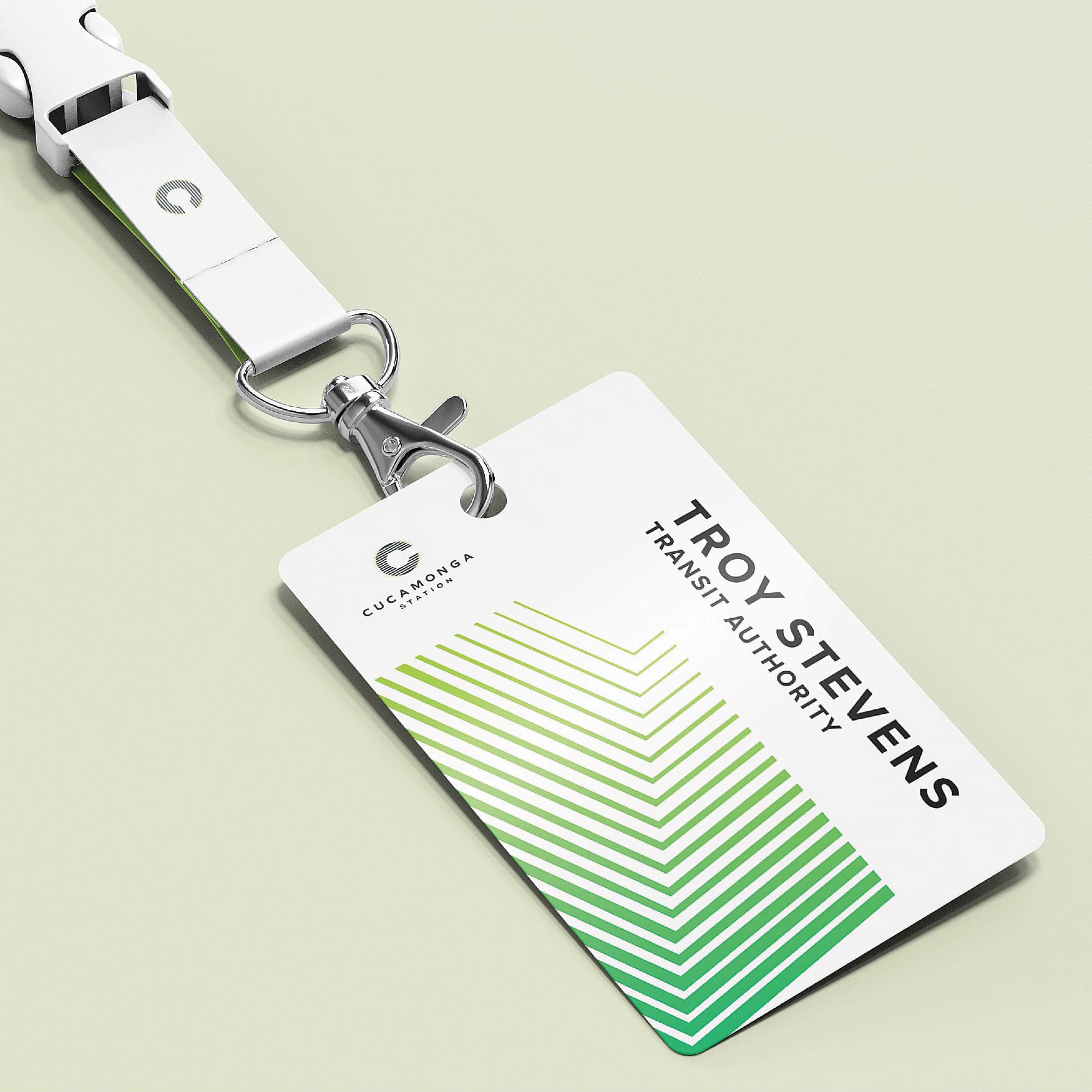 A Cucamonga Station Transit Authority staff ID badge and branded white lanyard displaying the "C" logomark, with the badge featuring a green gradient chevron stripe pattern, the Cucamonga Station wordmark, and a sample employee name — demonstrating RSM Design's branding and visual identity and print collateral services extended across all touchpoints within the transit market
