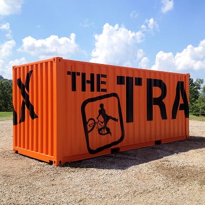 Branded orange shipping container with large-scale The Trax BMX activity signage and cyclist pictogram at Summit Bechtel Reserve, experiential environmental graphic design by RSM Design