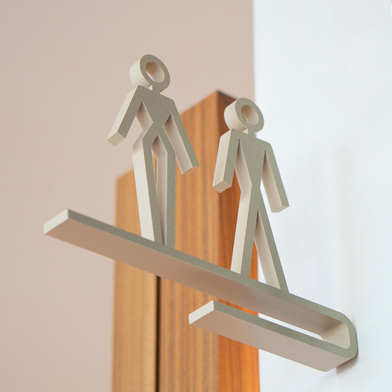 The Monarch at Hall Park custom restroom projecting sign — dimensional brushed metal male and female pictogram figures on horizontal blade sign mounted to wood door frame, interior wayfinding design by RSM Design