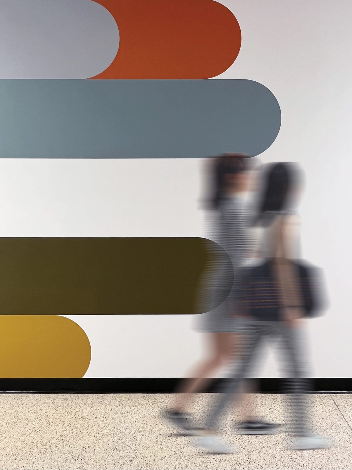 Students walking past bold abstract interior wall mural featuring stacked rounded rectangle forms in terracotta, teal, olive, and gold at University of Arkansas Windgate Arts and Design District