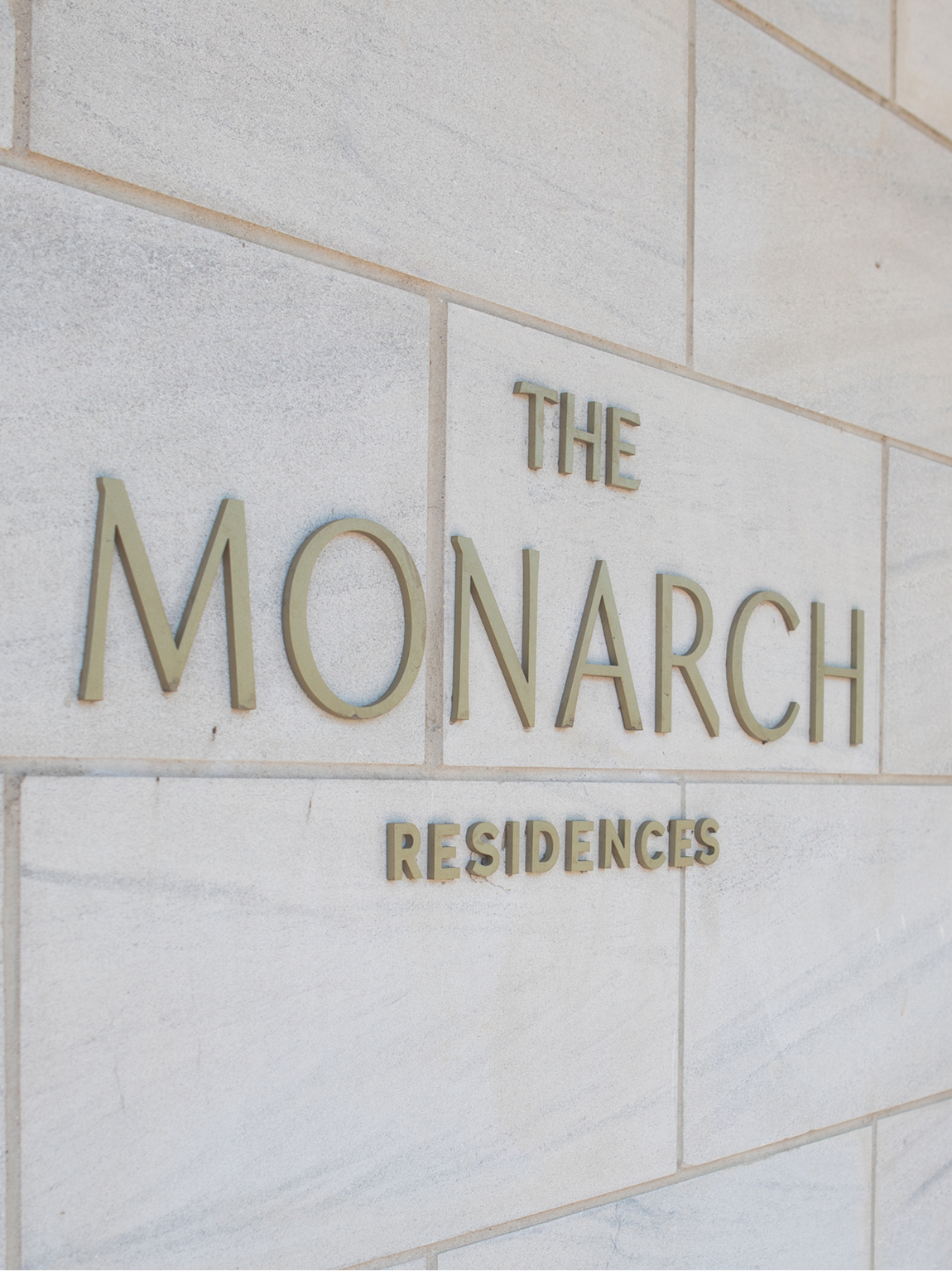 The Monarch Residences dimensional bronze building signage mounted on limestone exterior wall — luxury residential wayfinding and environmental graphic design by RSM Design, Frisco Texas