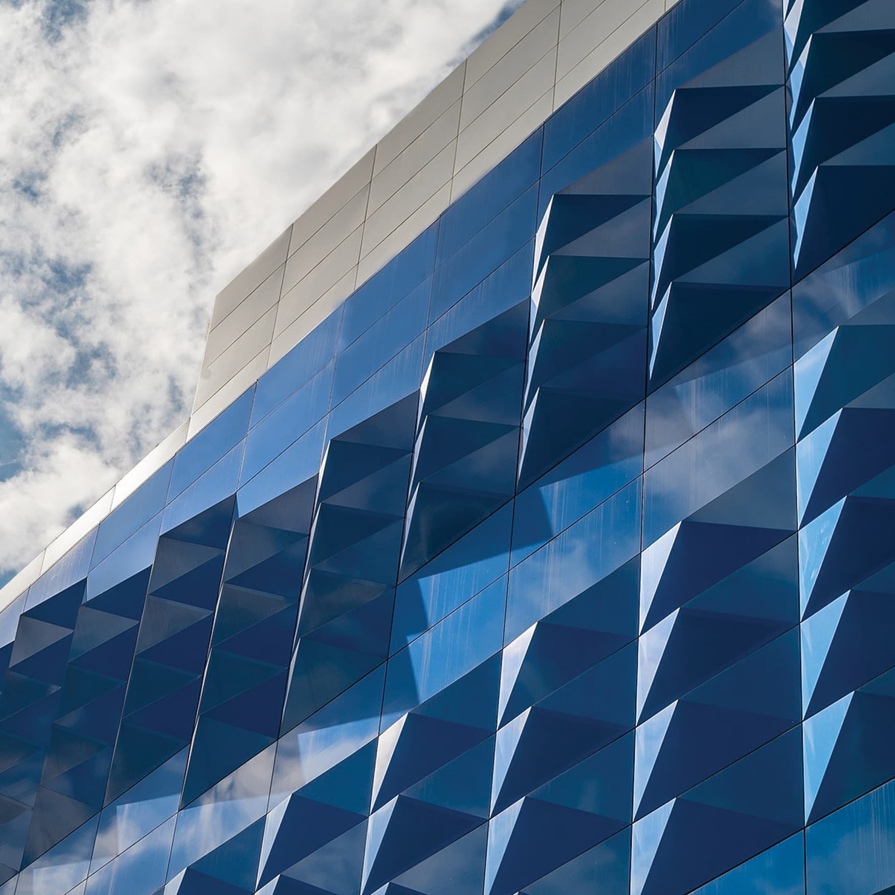 Geometric building facade design in reflective blue with clouds in the sky
