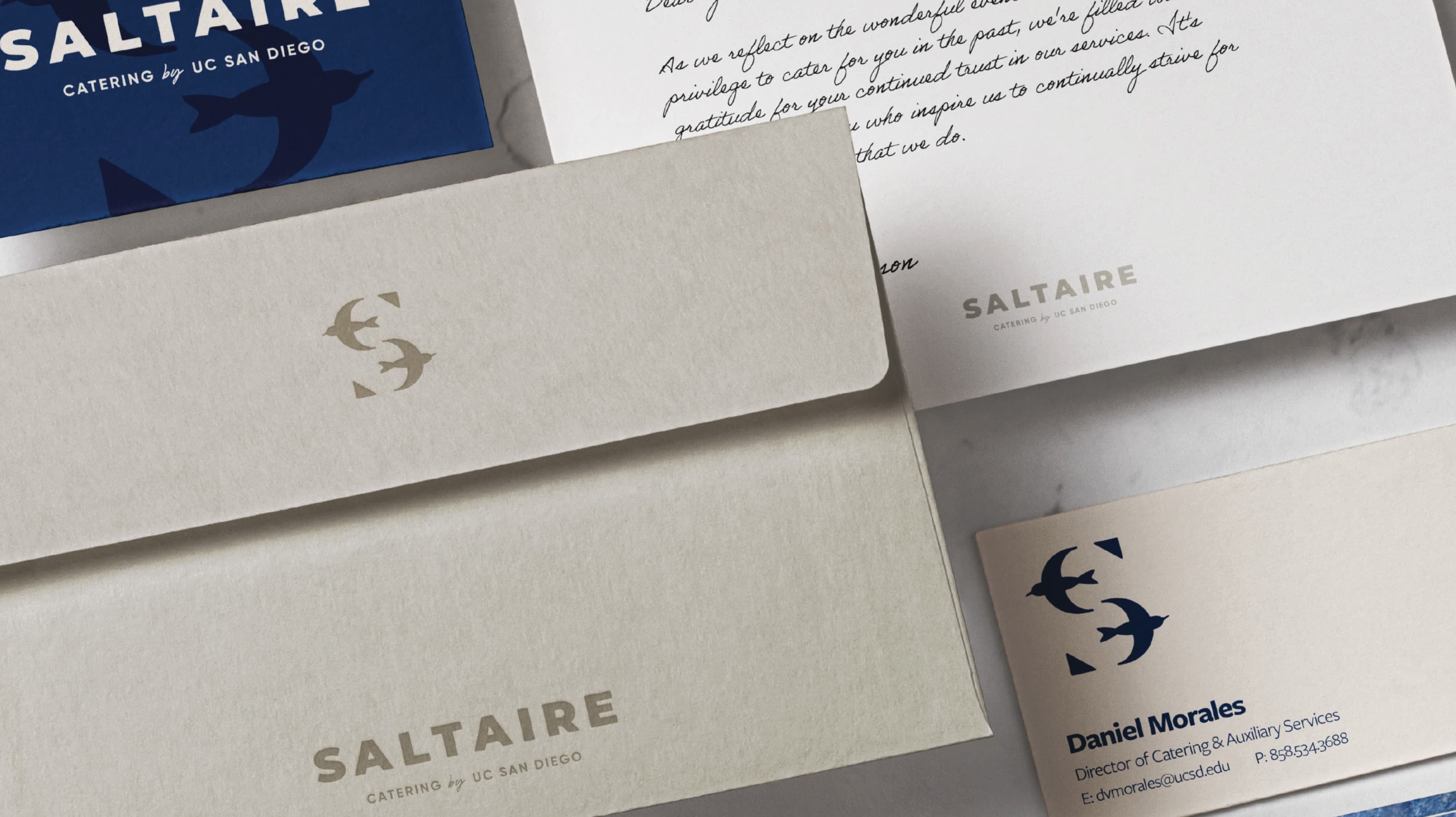 Saltaire Catering by UC San Diego branded stationery suite including envelopes, letterhead, and business cards featuring the tern lettermark in navy and sand, showcasing print collateral and visual identity design for a food and beverage and education market client by RSM Design.