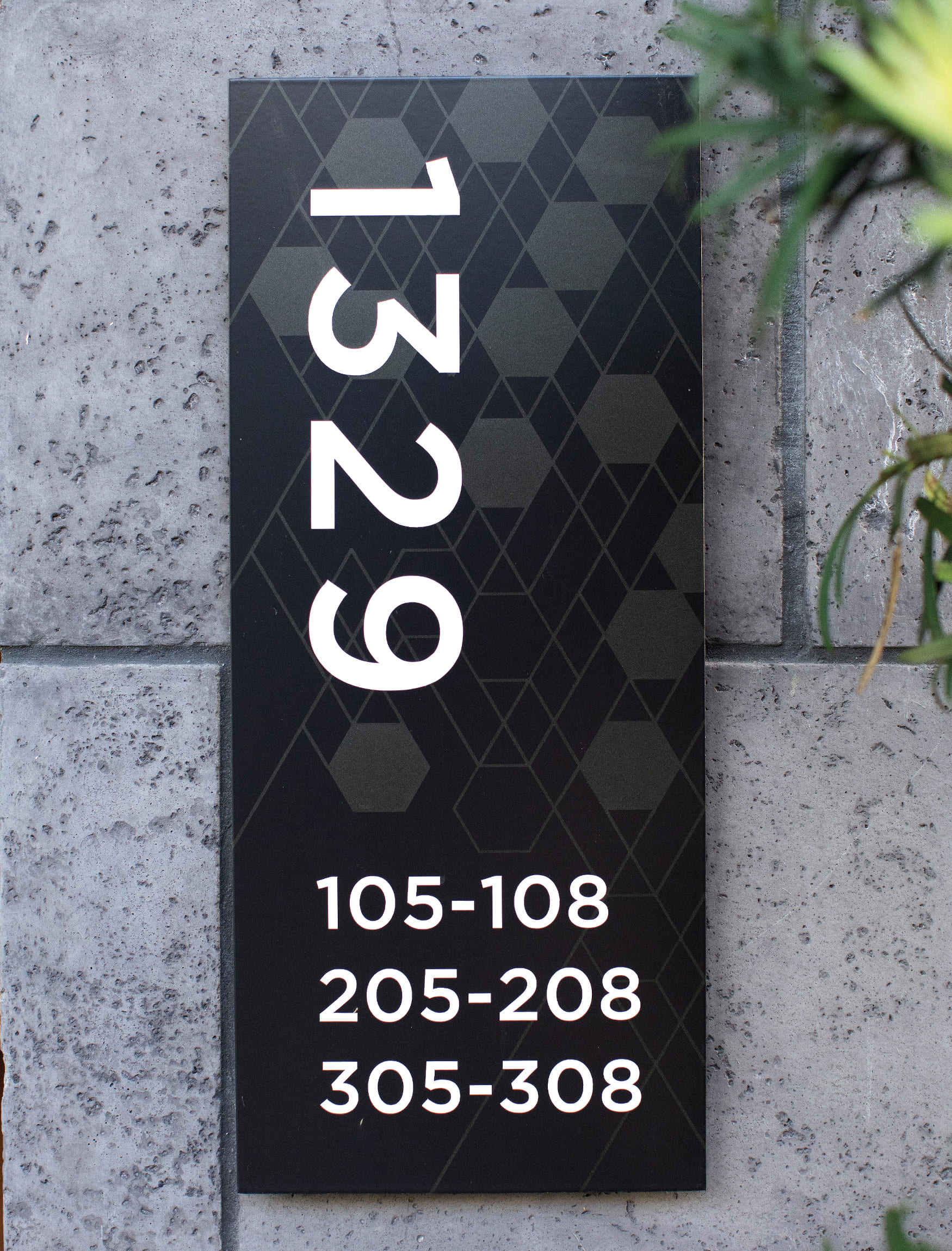 Black veritcal wall mounted building information plaque with unit numbers and building number in white and printed tonal grey hexagonal pattern. Signage and wayfinding for Persea in San Diego, California by RSM Design