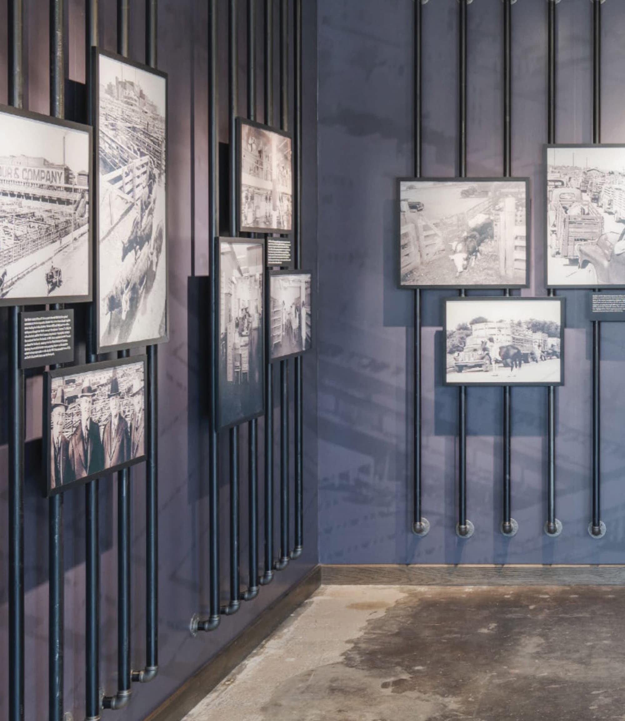 A wall installation of images mounted to industrial vertical pipes with the history of the building in a timeline format.
