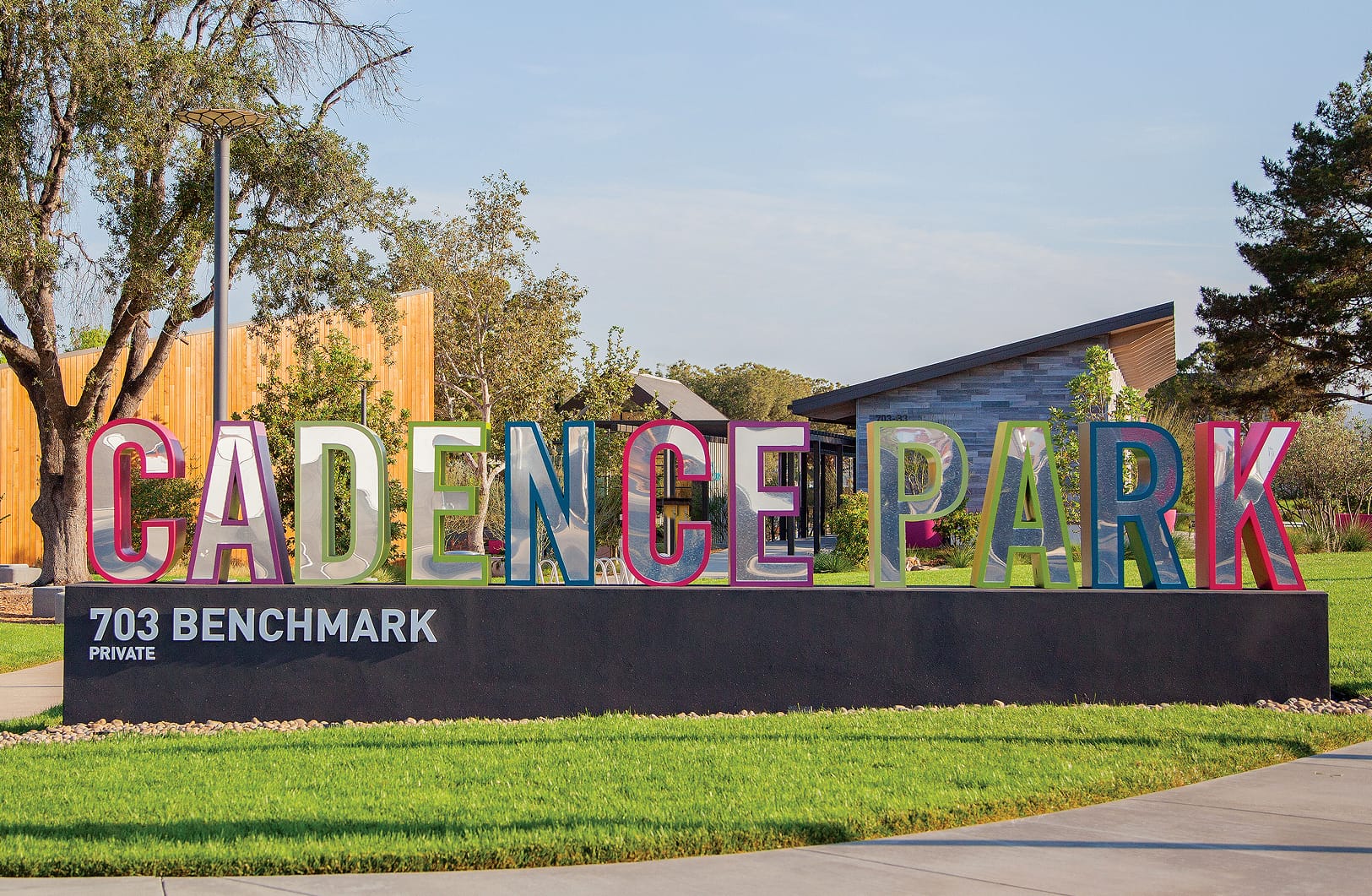 Large-scale dimensional "Cadence Park" monument sign with polished mirrored letters outlined in multicolor pink, teal, and green mounted on a dark concrete base at 703 Benchmark Private in Irvine, California, designed by RSM Design