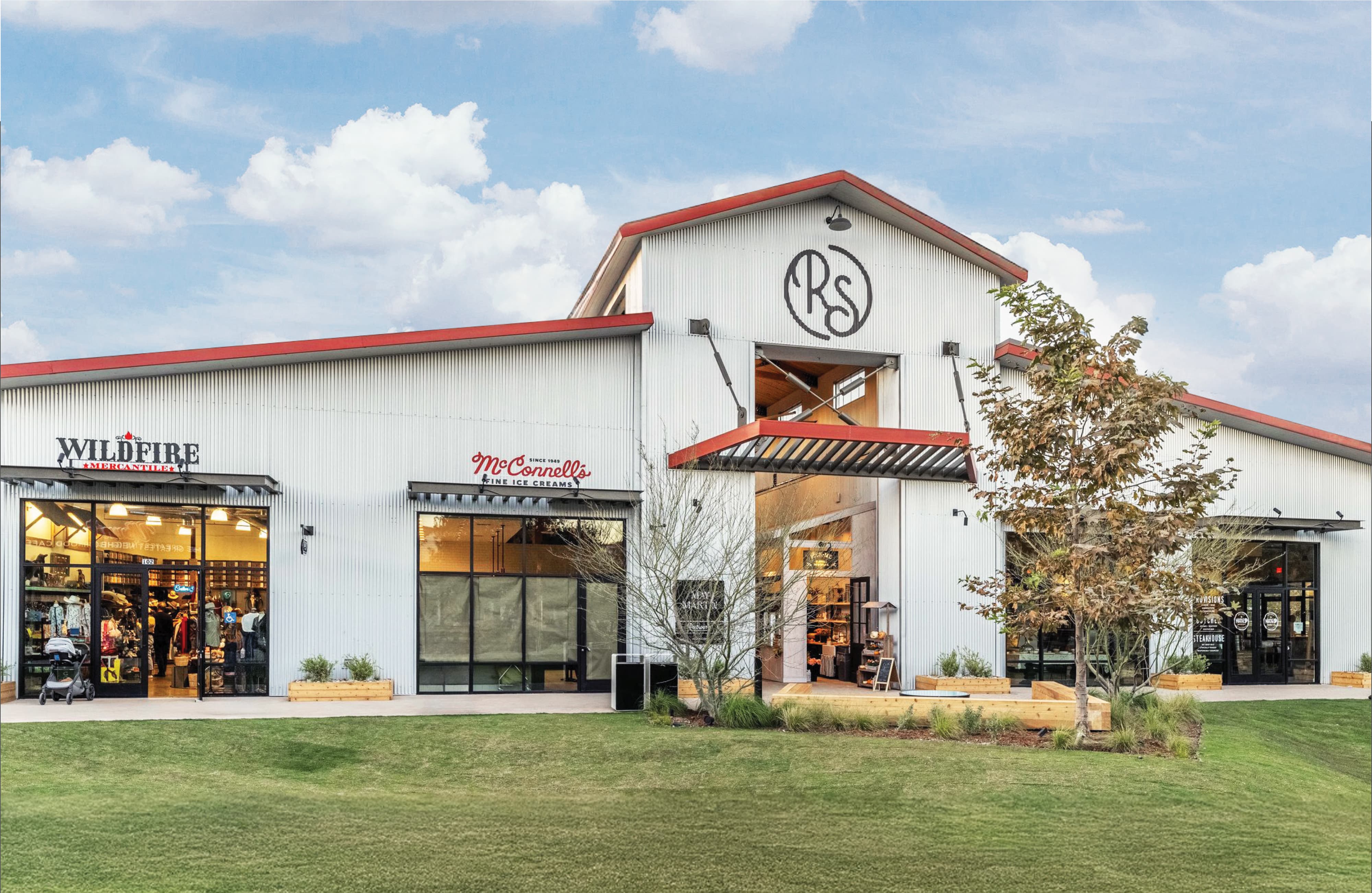 Exterior of River Street Market, a corrugated metal barn-style retail building featuring tenant signage for Wildfire Mercantile and McConnell's Fine Ice Creams with a large "RS" monogram logo painted on the gabled facade, showcasing master sign program and branded environment design for a mixed-use retail and food and beverage environment by RSM Design.