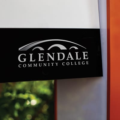 Close-up of Glendale Community College logo on illuminated wayfinding pylon sign designed by RSM Design, featuring silver dimensional lettering on a dark panel with orange frame detail
