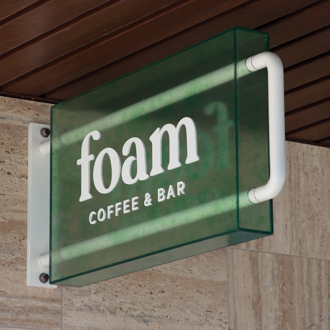 Foam Coffee and Bar green glass blade sign mounted on travertine facade at Wai Kai, Ewa Beach, Oahu, environmental graphic design by RSM Design.